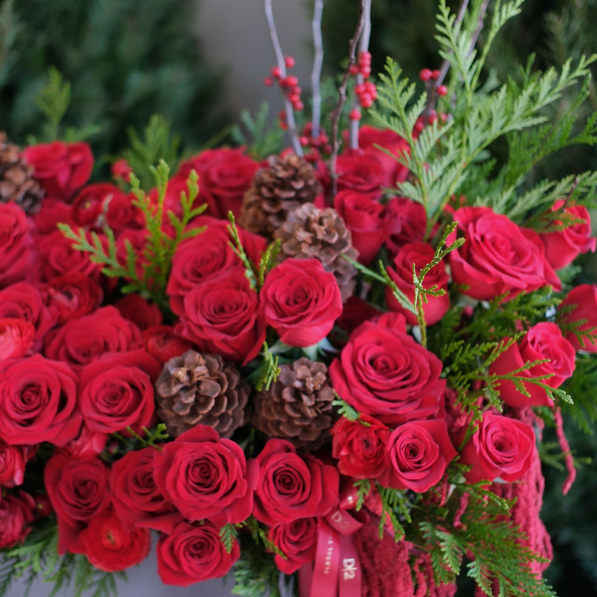 A lush display of red roses, evergreens, pinecones, and berries arranged in