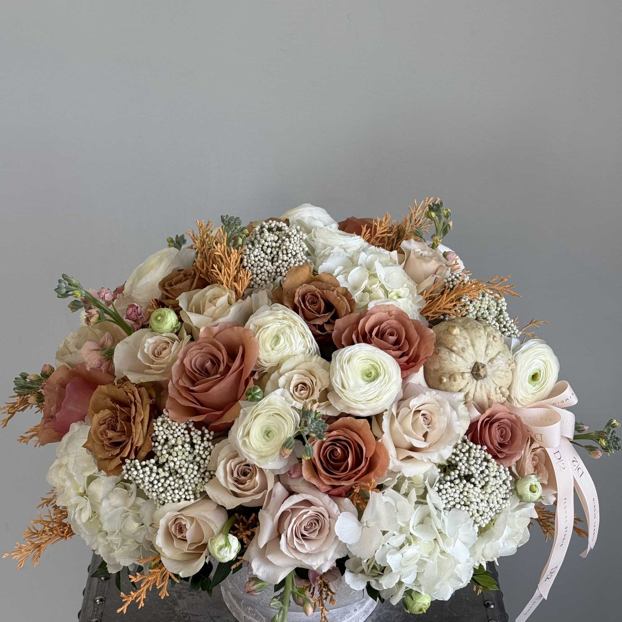Warm neutral roses, hydrangeas, and seasonal textures arranged in a stone bowl