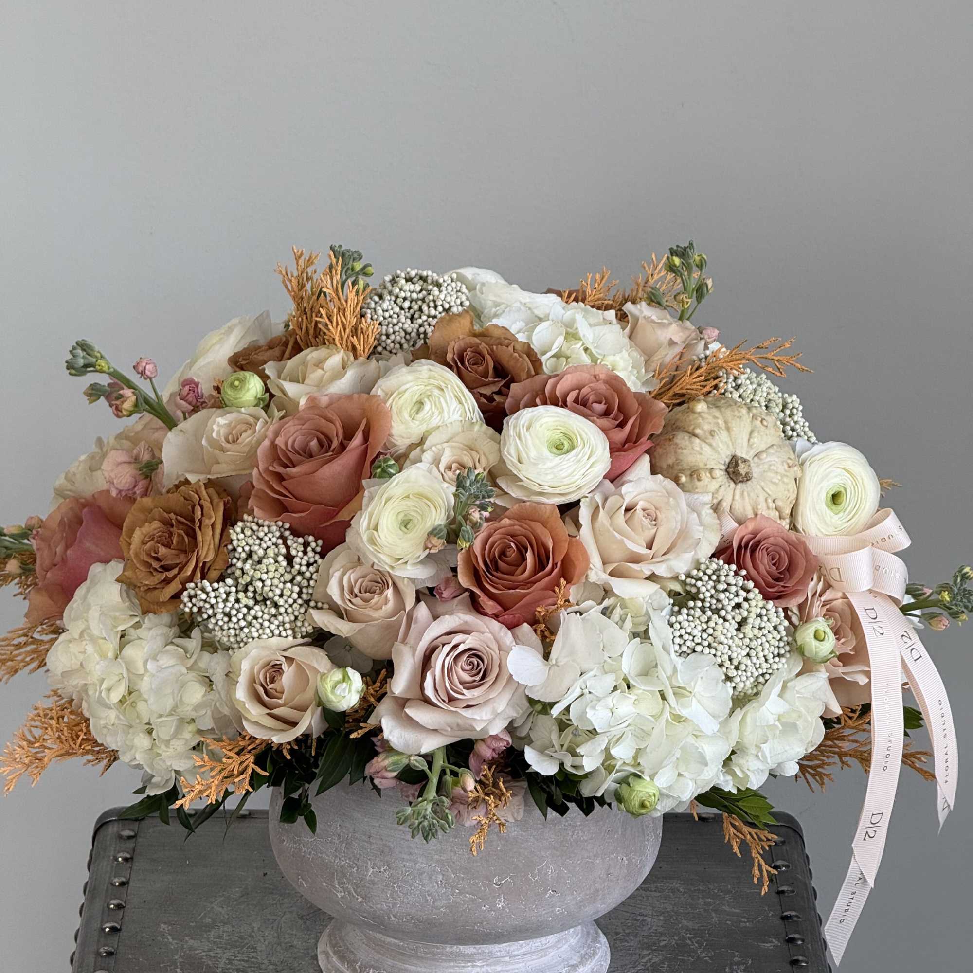 Warm neutral roses, hydrangeas, and seasonal textures arranged in a stone bowl