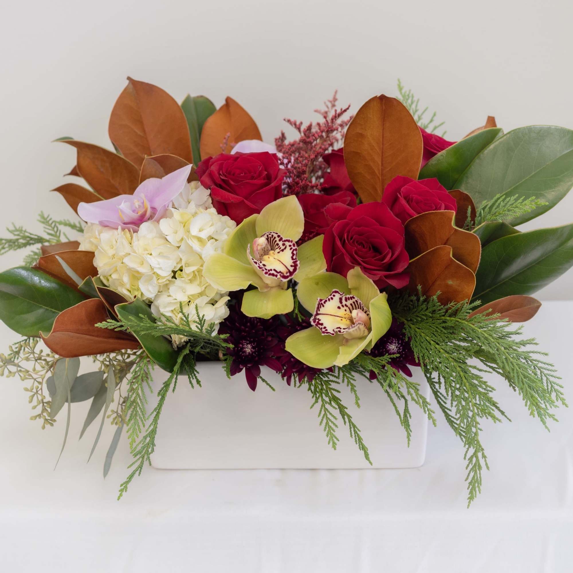 A lush seasonal centerpiece featuring vibrant red roses, green cymbidium orchids, soft