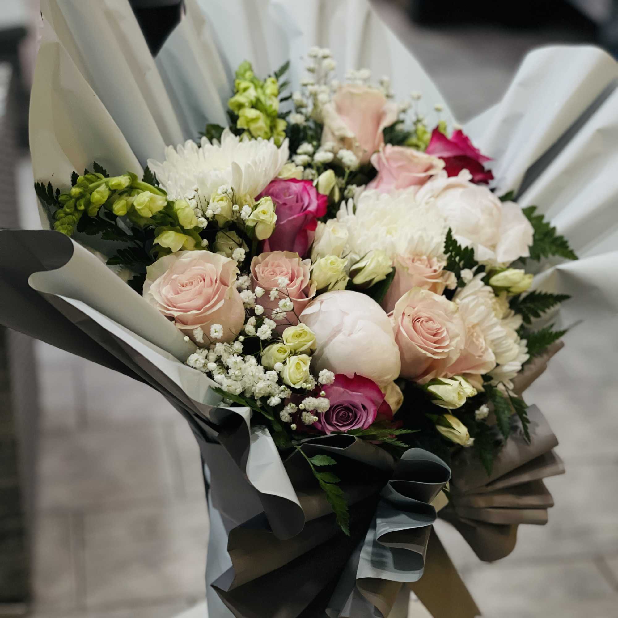 is a soft, romantic arrangement crafted with premium blush roses, white spray