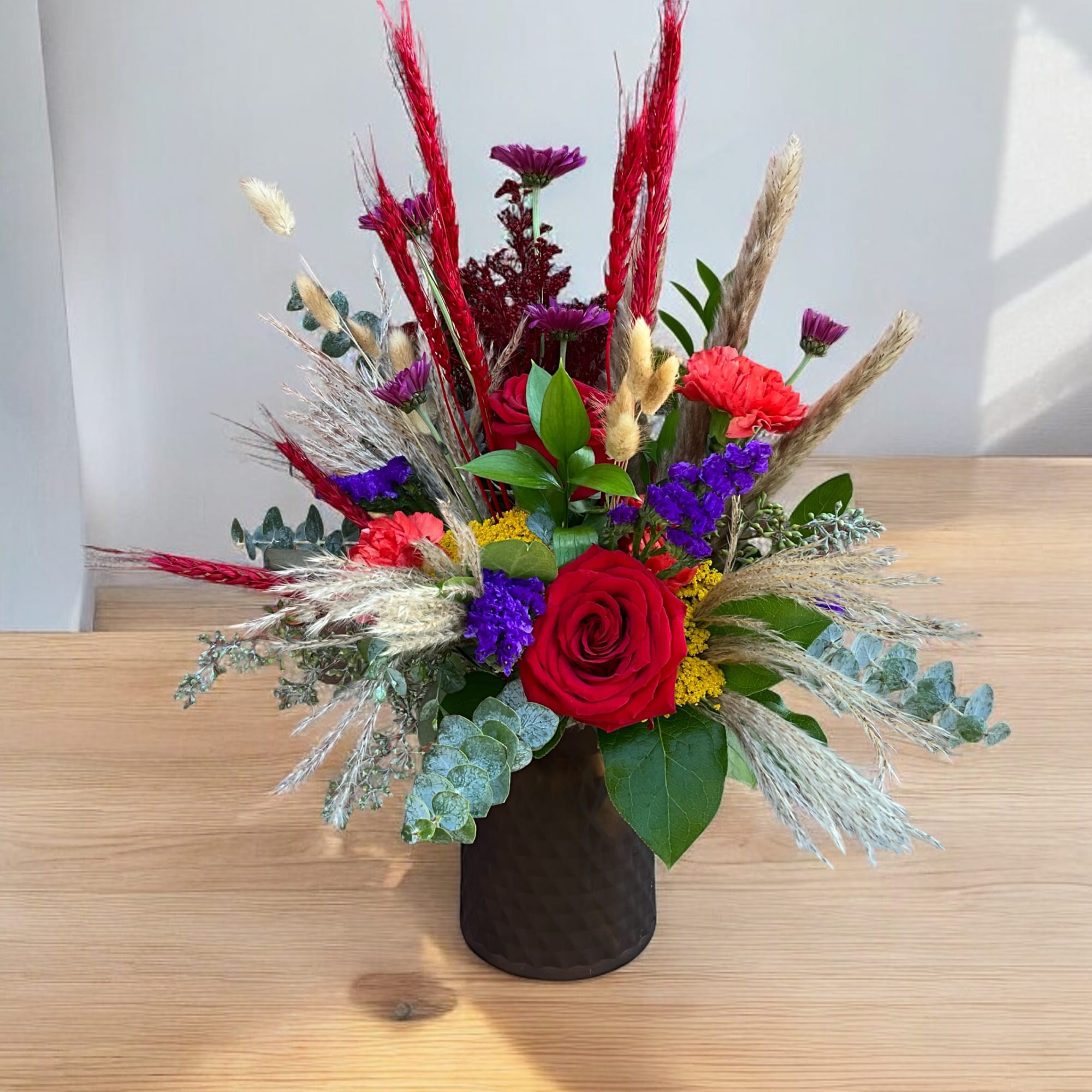 This bouquet features vibrant jewel tones arranged in a complimentary glass vase.