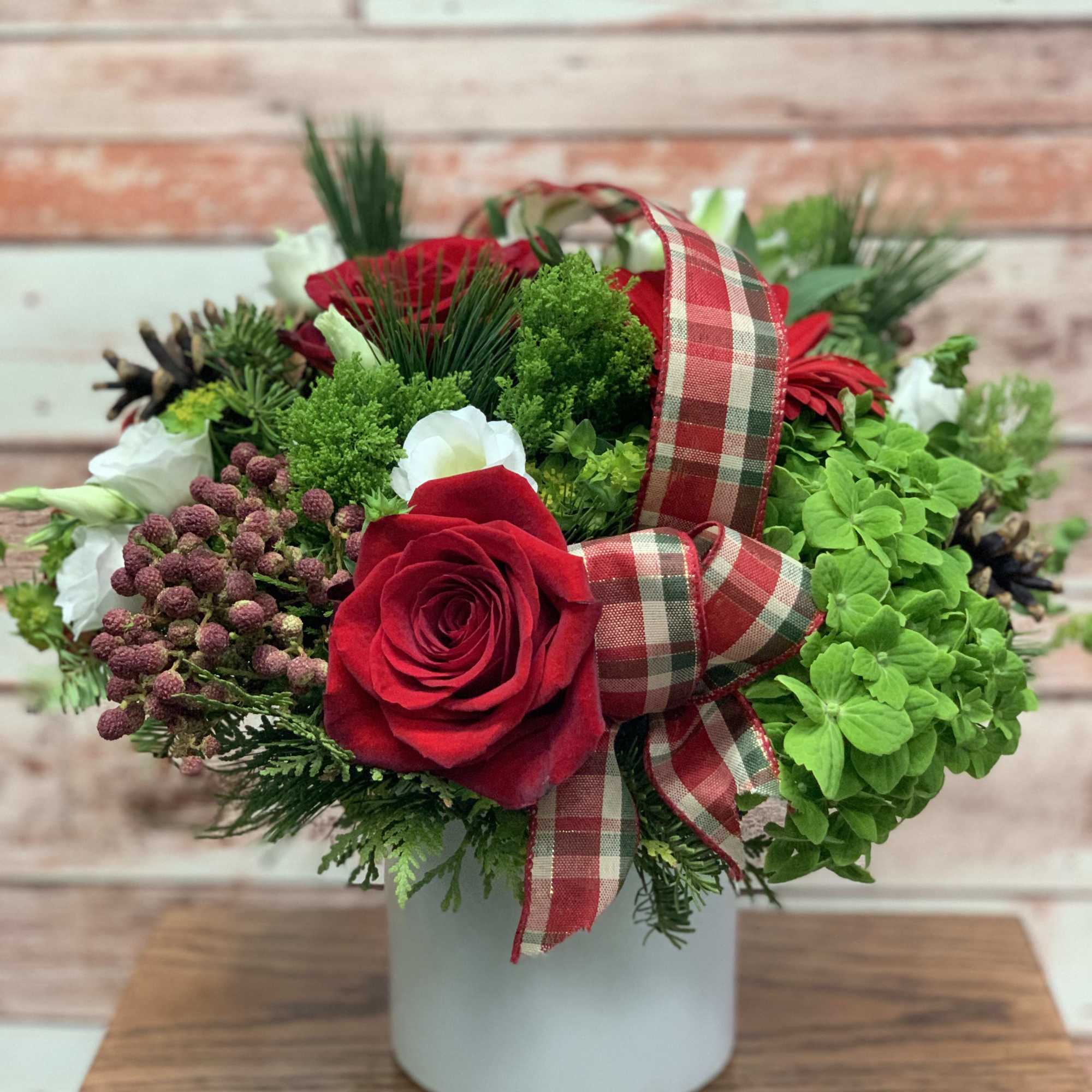 A festive red and green arrangement with decorative ribbon and pine cones.