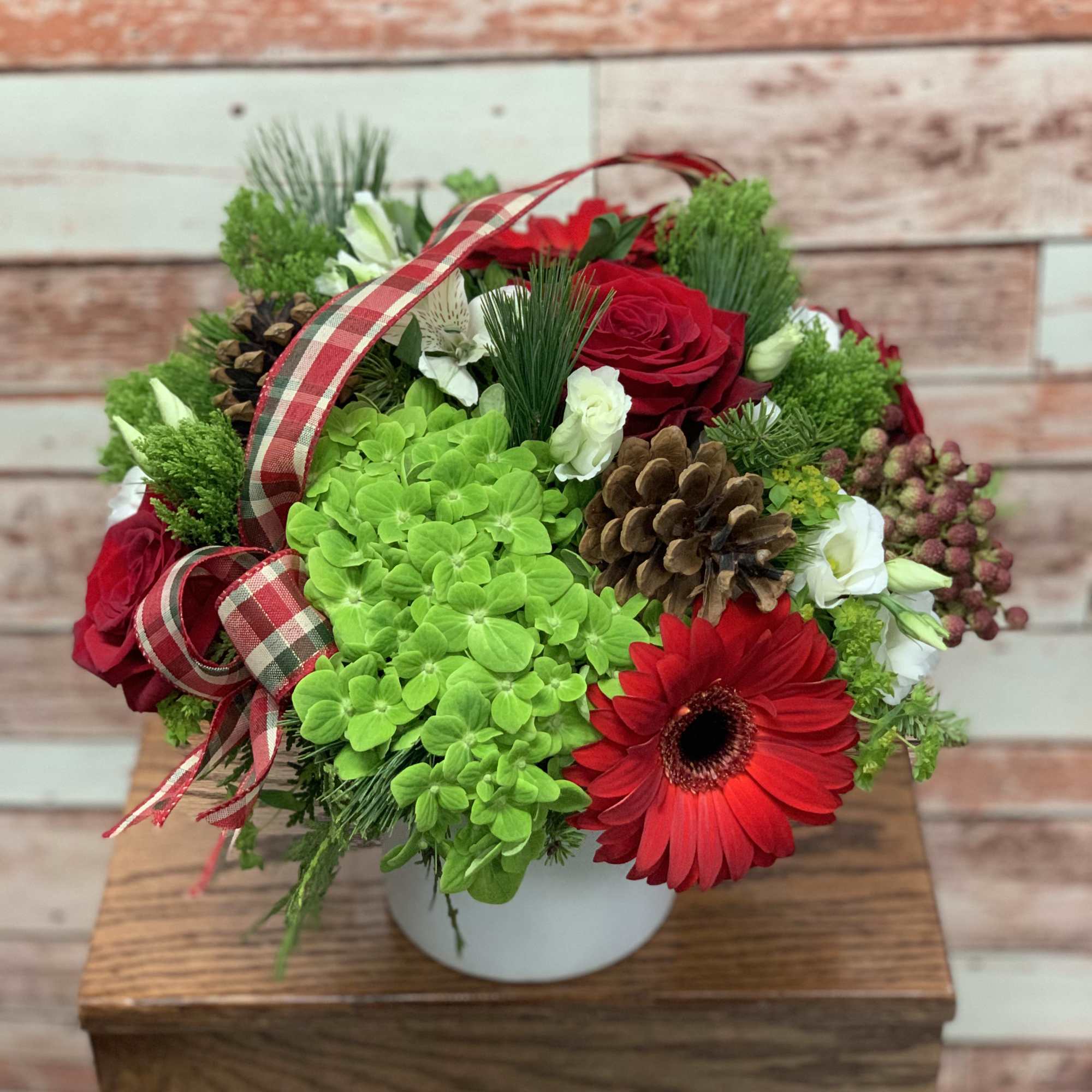 A festive red and green arrangement with decorative ribbon and pine cones.