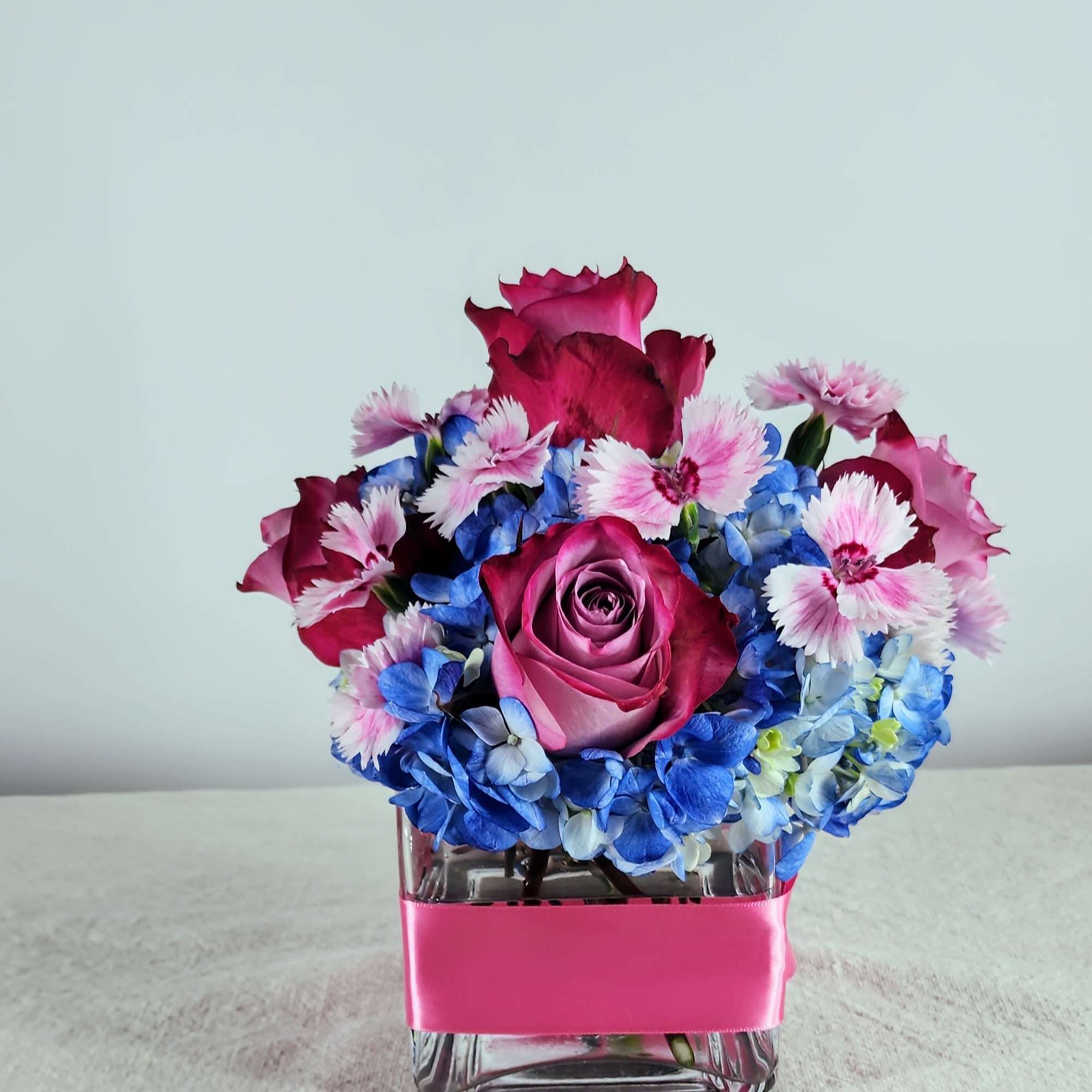 Blue hydrangeas, spray roses, miniature carnations &amp; dianthus fill this cube vase.