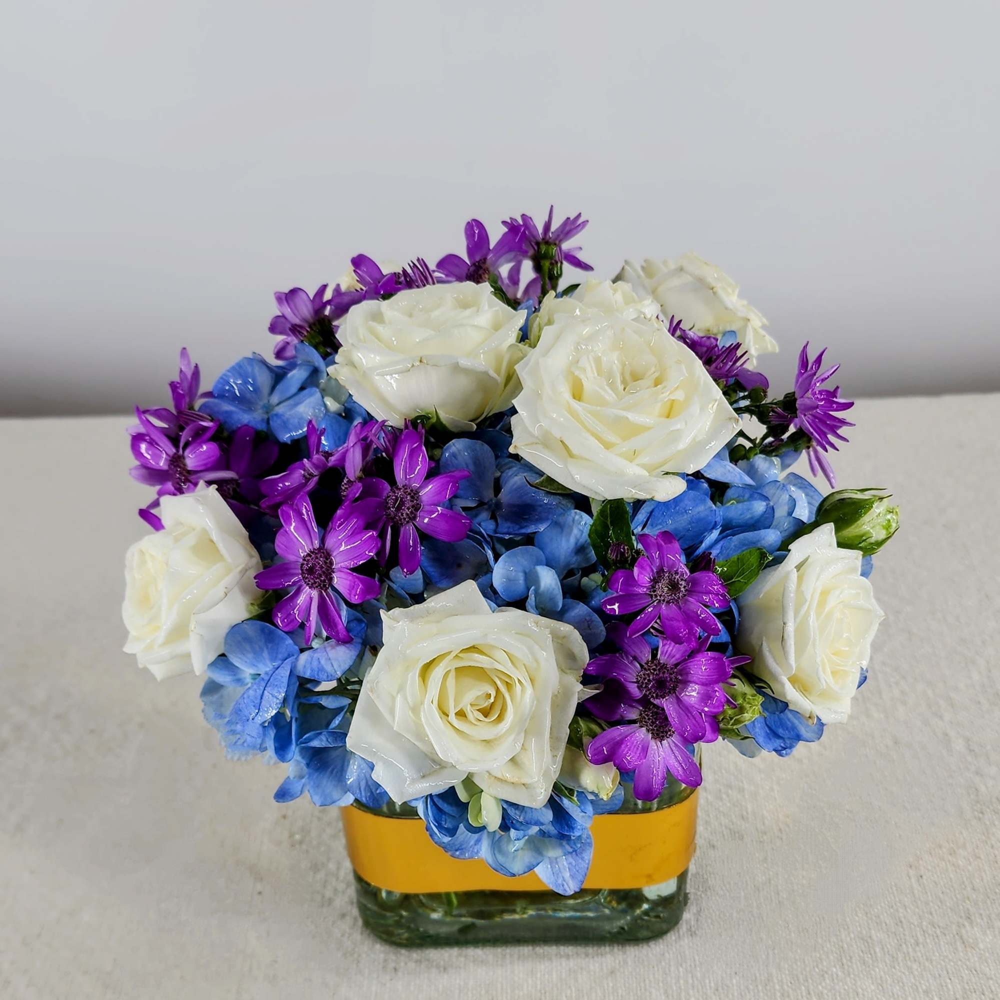 Blue hydrangeas, spray roses, miniature carnations &amp; dianthus fill this cube vase.