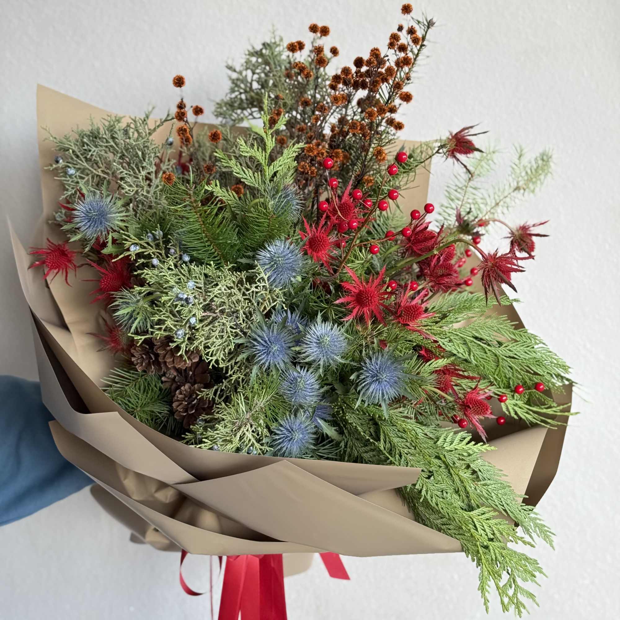 A festive and modern handheld holiday bouquet featuring striking blue and red