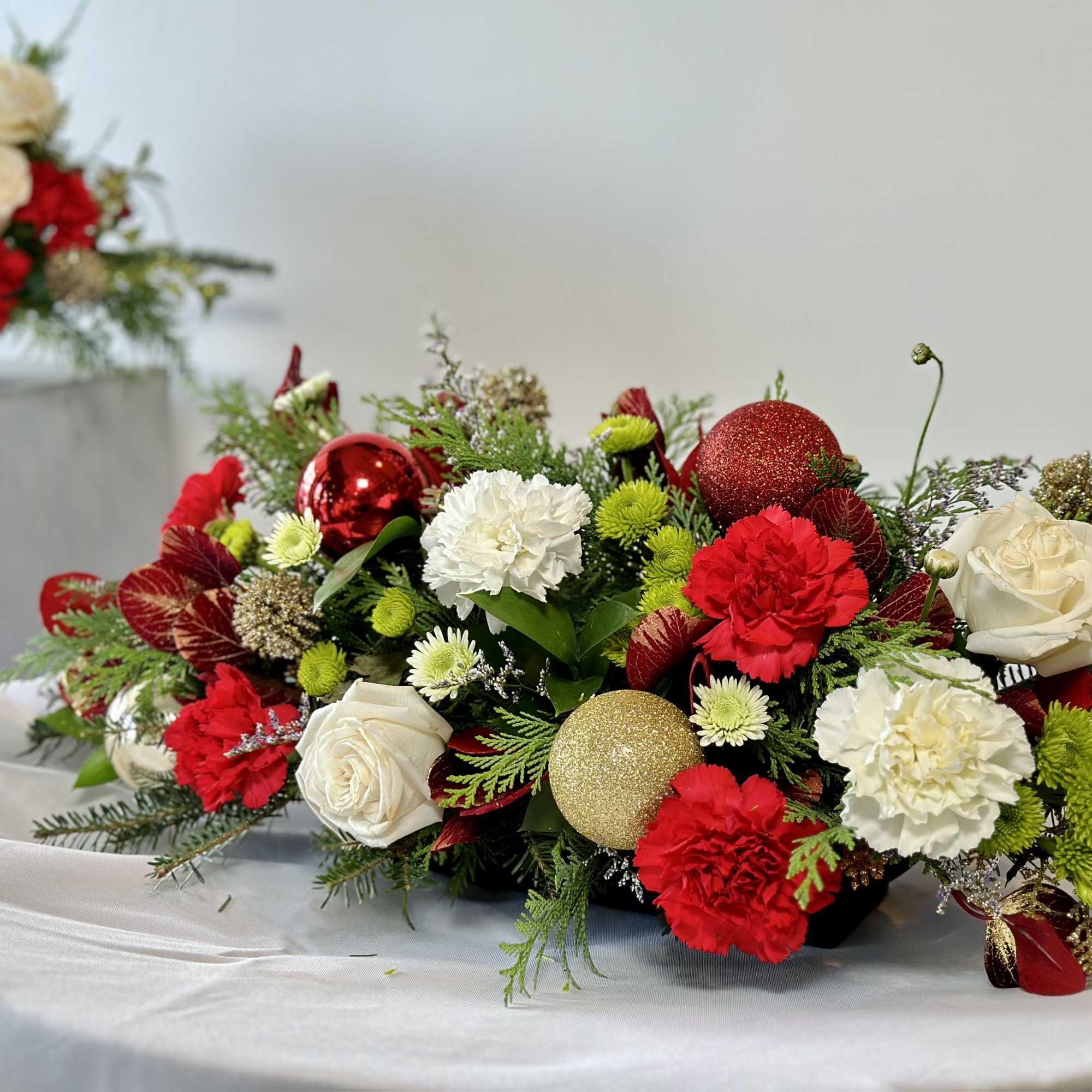 A Christmas centerpiece with fresh cut flowers, greenery, ornaments and ribbon to
