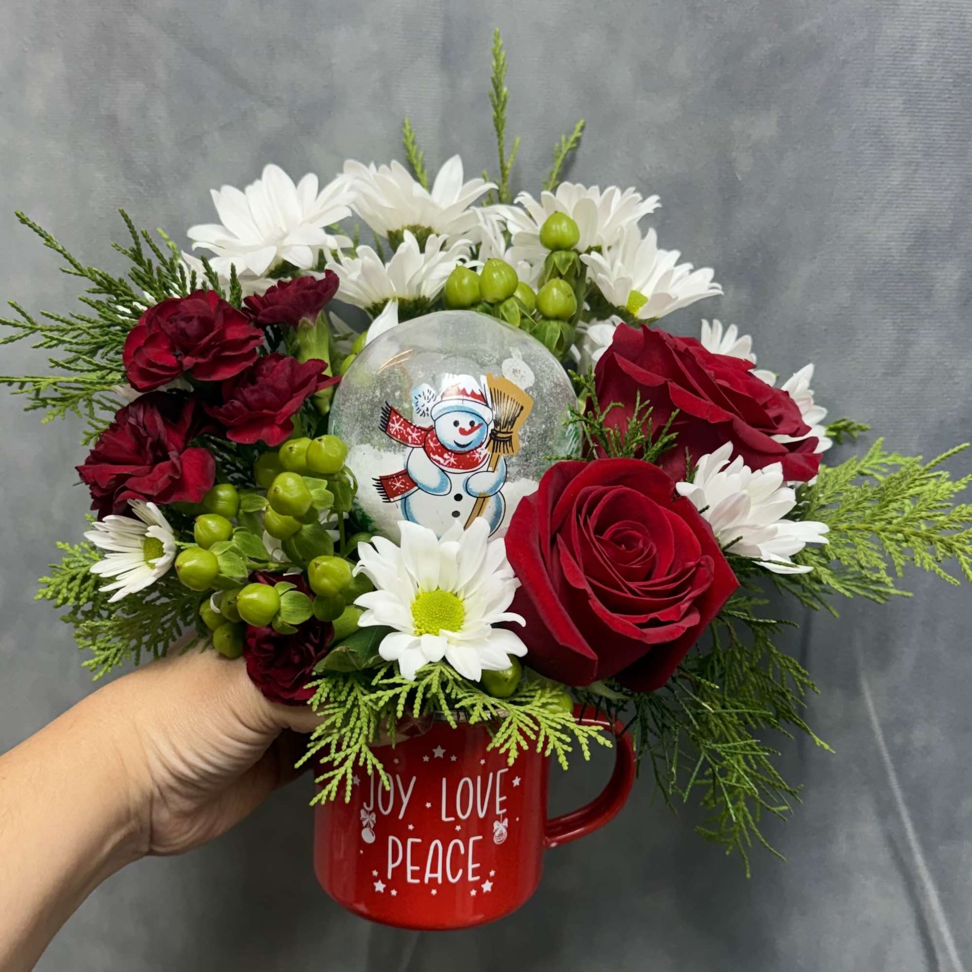 A festive Christmas mug filled with fresh red roses, white daisies, holiday