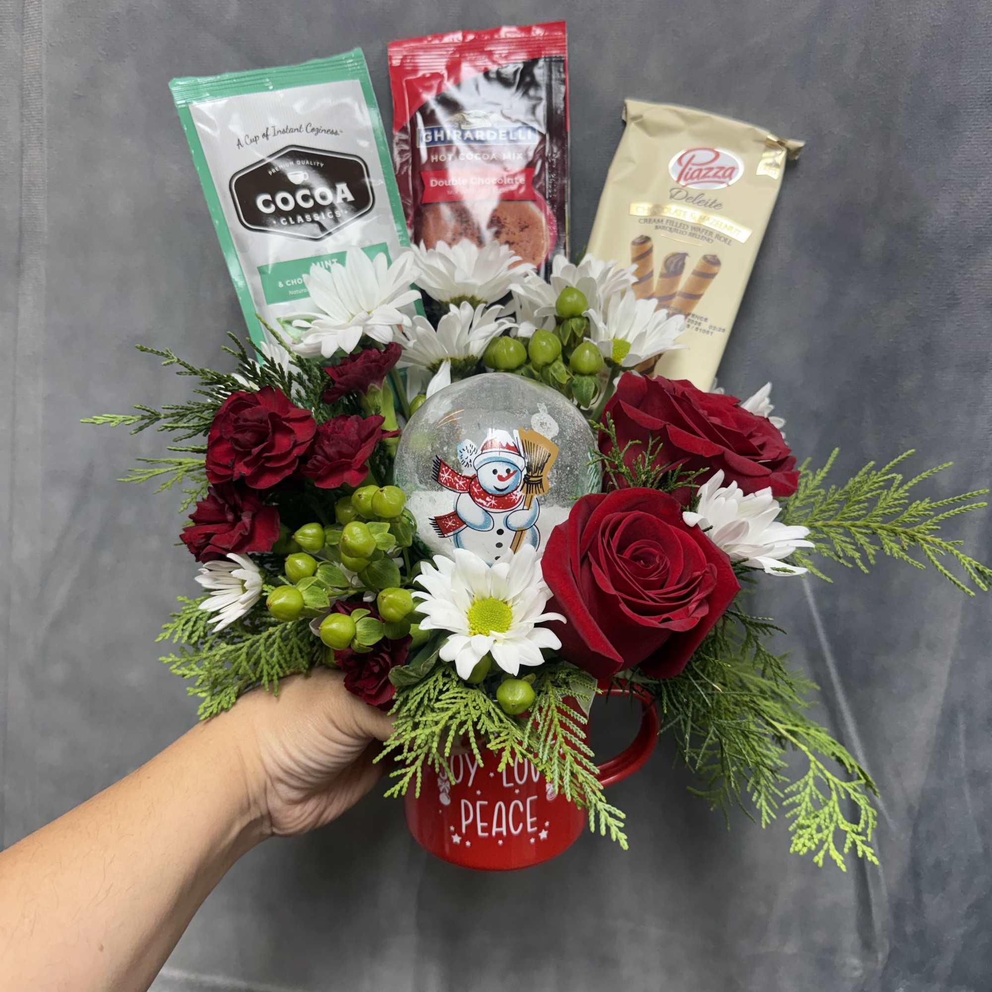 A festive Christmas mug filled with fresh red roses, white daisies, holiday