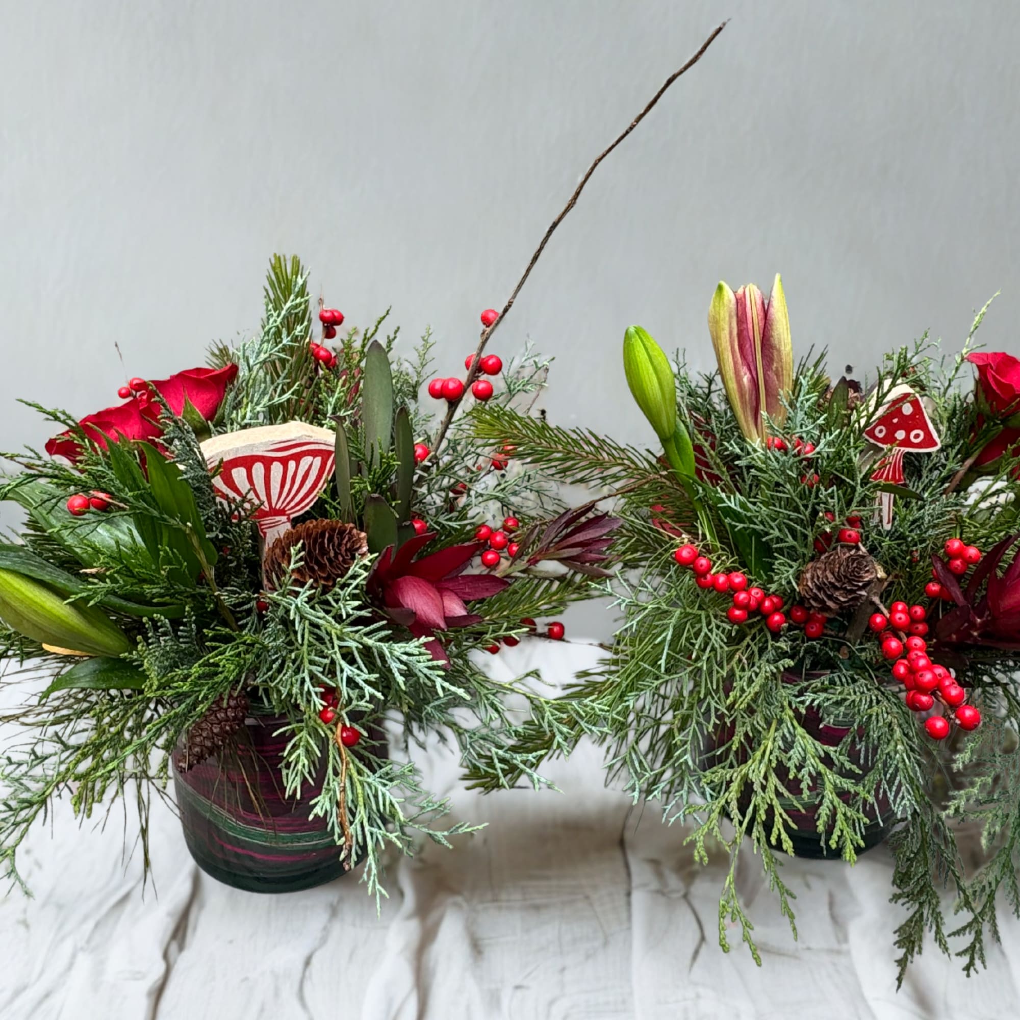A cheerful holiday arrangement featuring rich evergreens, vibrant red roses, winterberries, and
