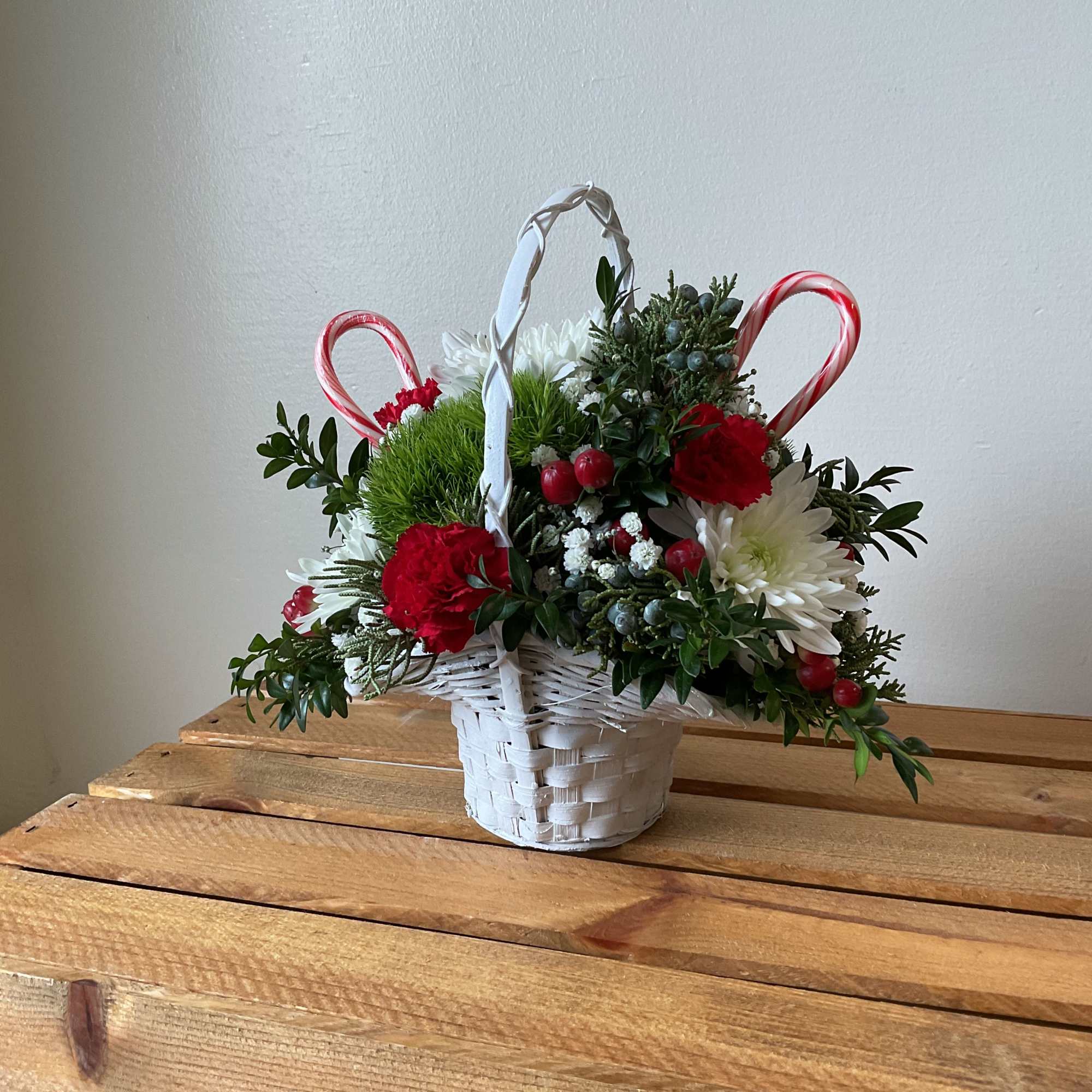 Small white handled basket finned with Christmas greens along with green, red