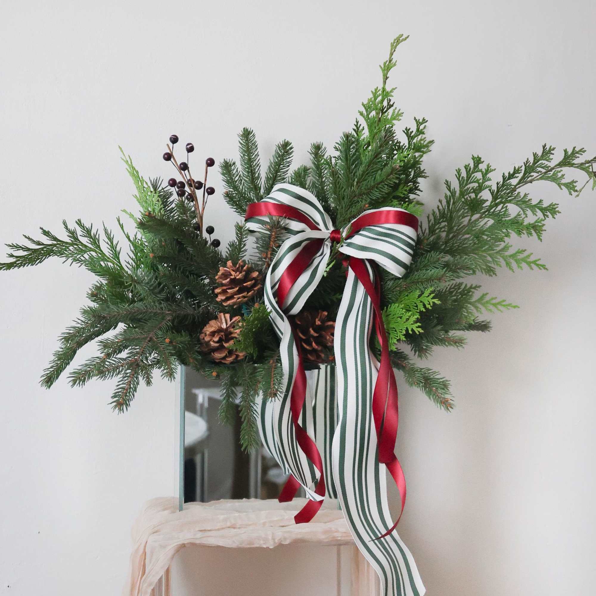 A keepsake mirror vase with fragrant seasonal greens and pinecones adorned with