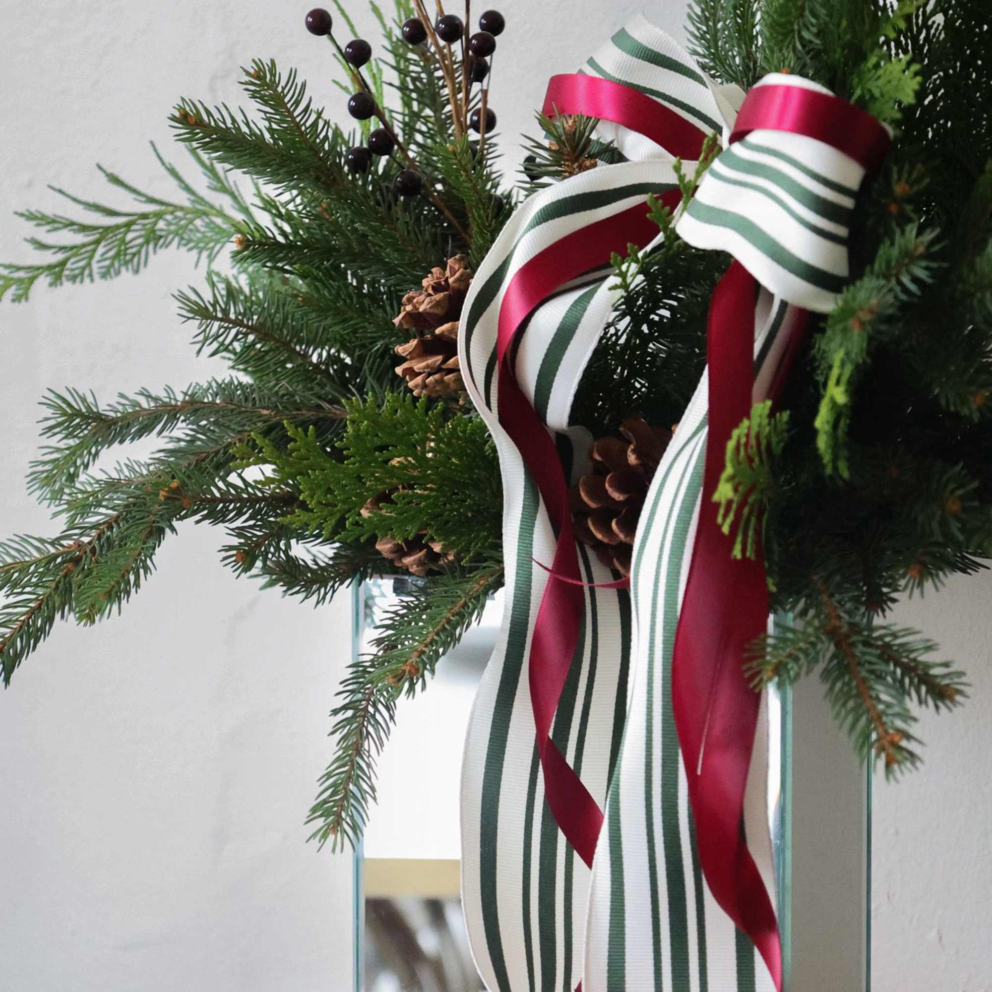 A keepsake mirror vase with fragrant seasonal greens and pinecones adorned with