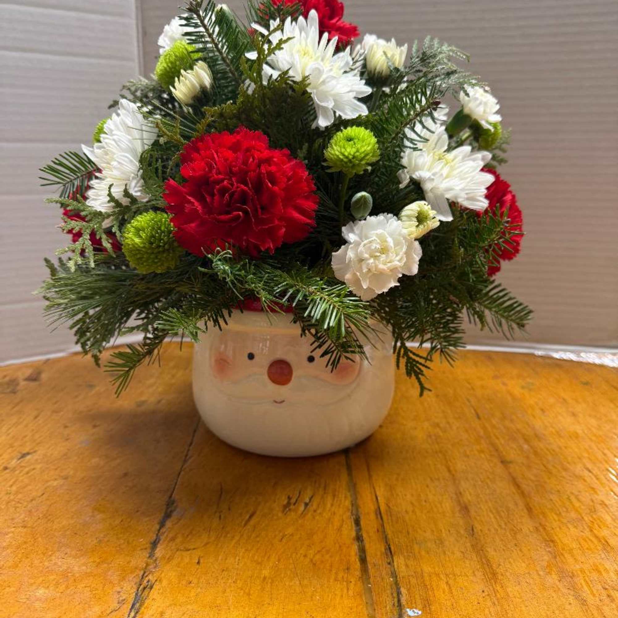 Ceramic Santa Face container filled with various Christmas greens, red carnations, green