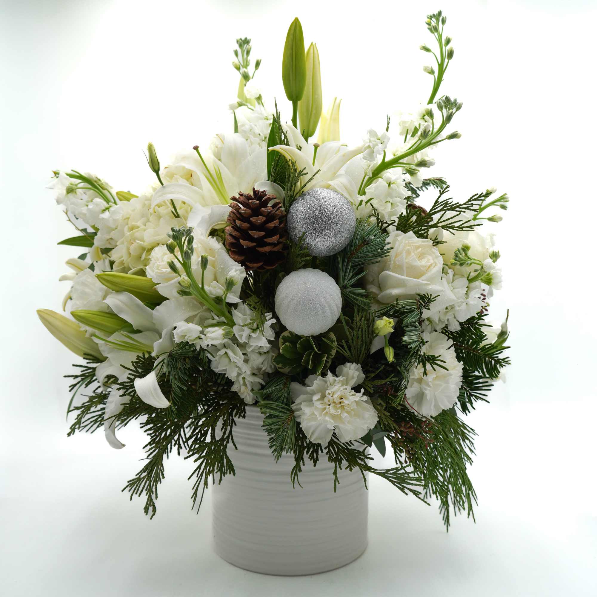 A beautiful winter-inspired arrangement featuring elegant white blooms, seasonal evergreens, pinecones, and