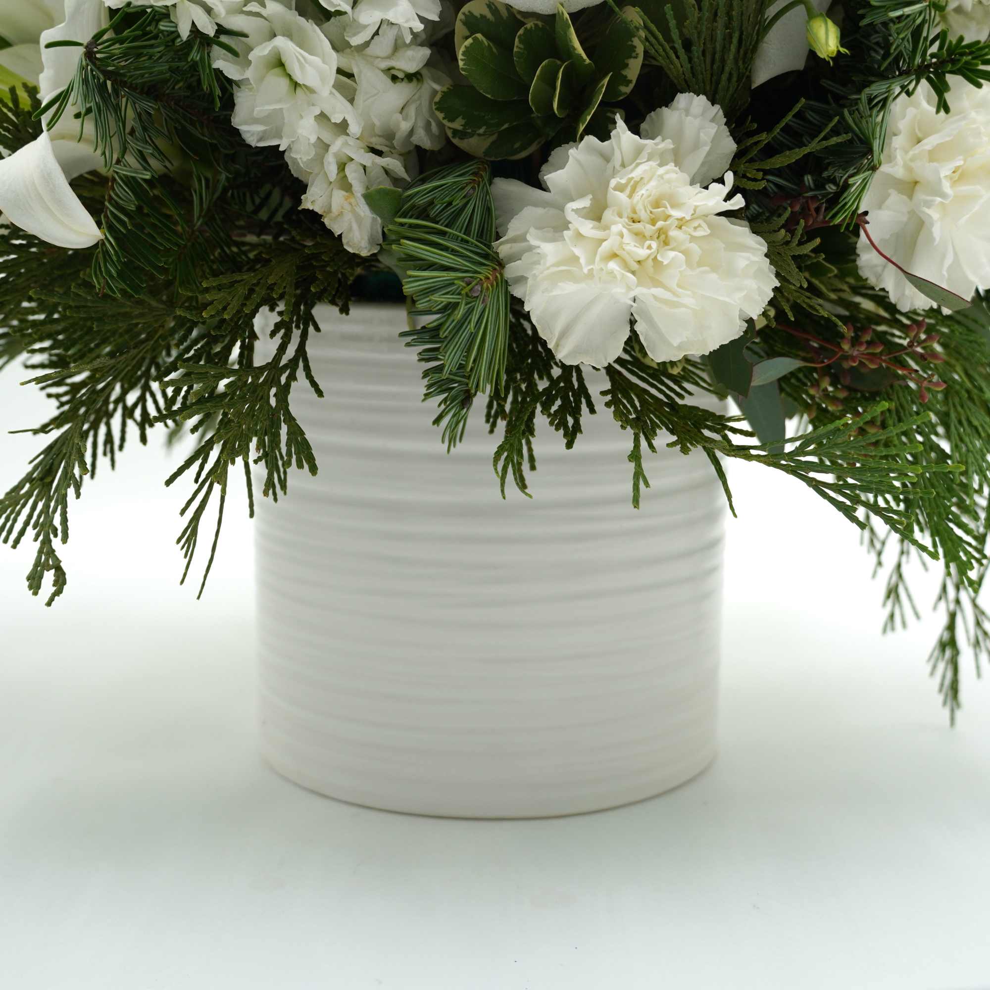 A beautiful winter-inspired arrangement featuring elegant white blooms, seasonal evergreens, pinecones, and