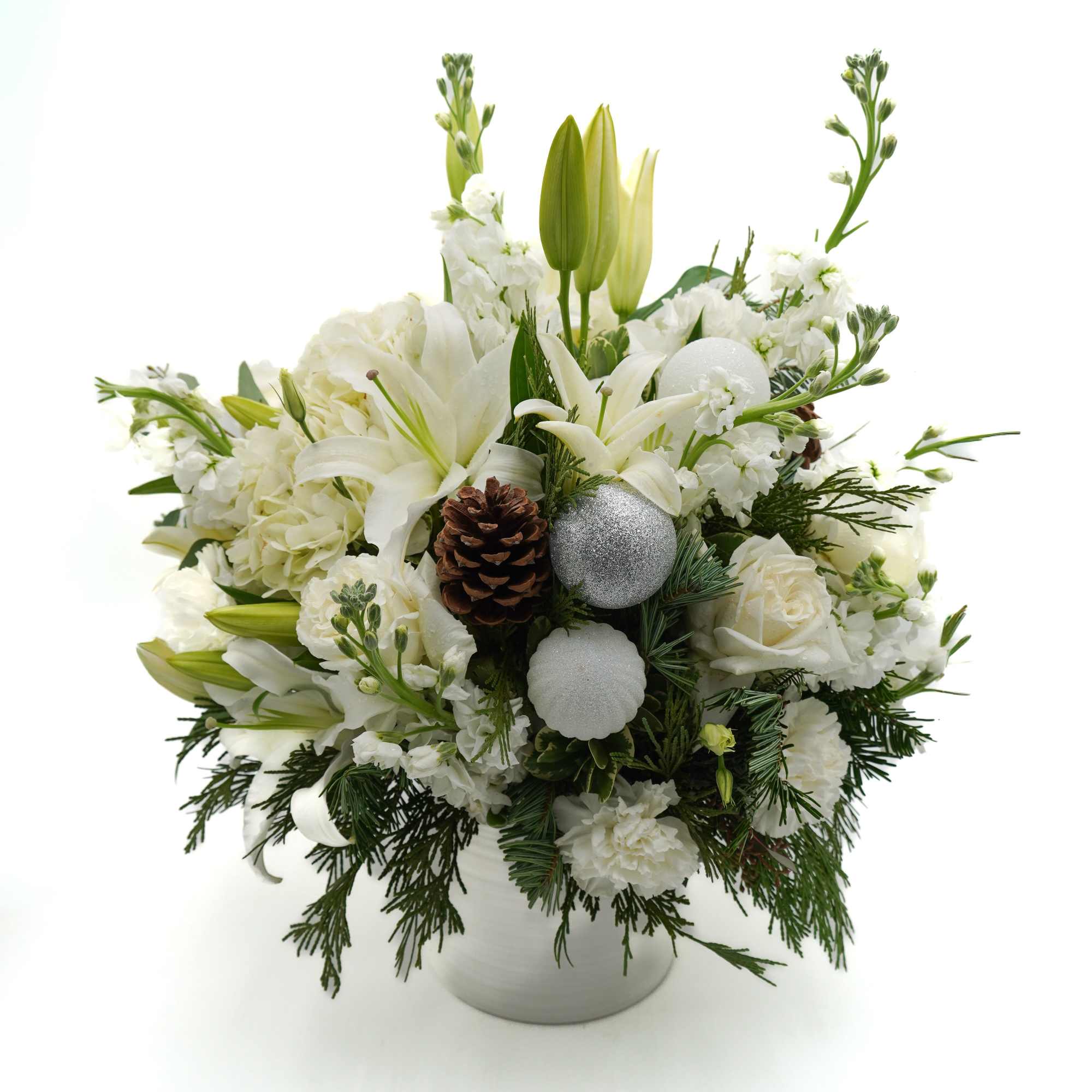A beautiful winter-inspired arrangement featuring elegant white blooms, seasonal evergreens, pinecones, and