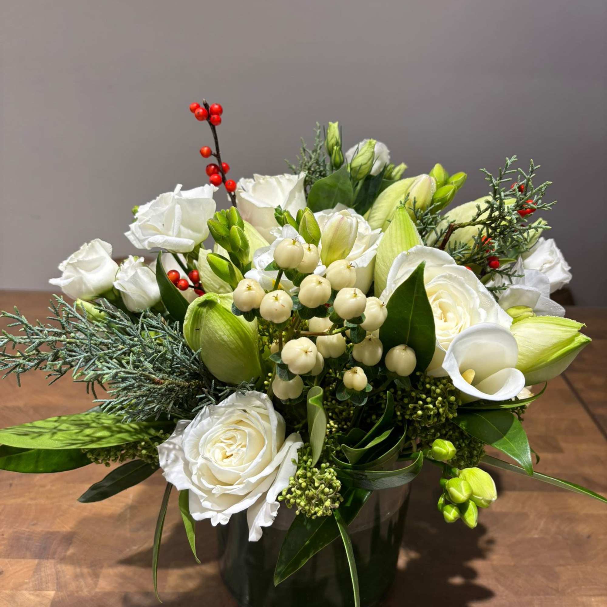 A fresh winter-inspired arrangement featuring elegant white roses, calla lilies, hypericum berries