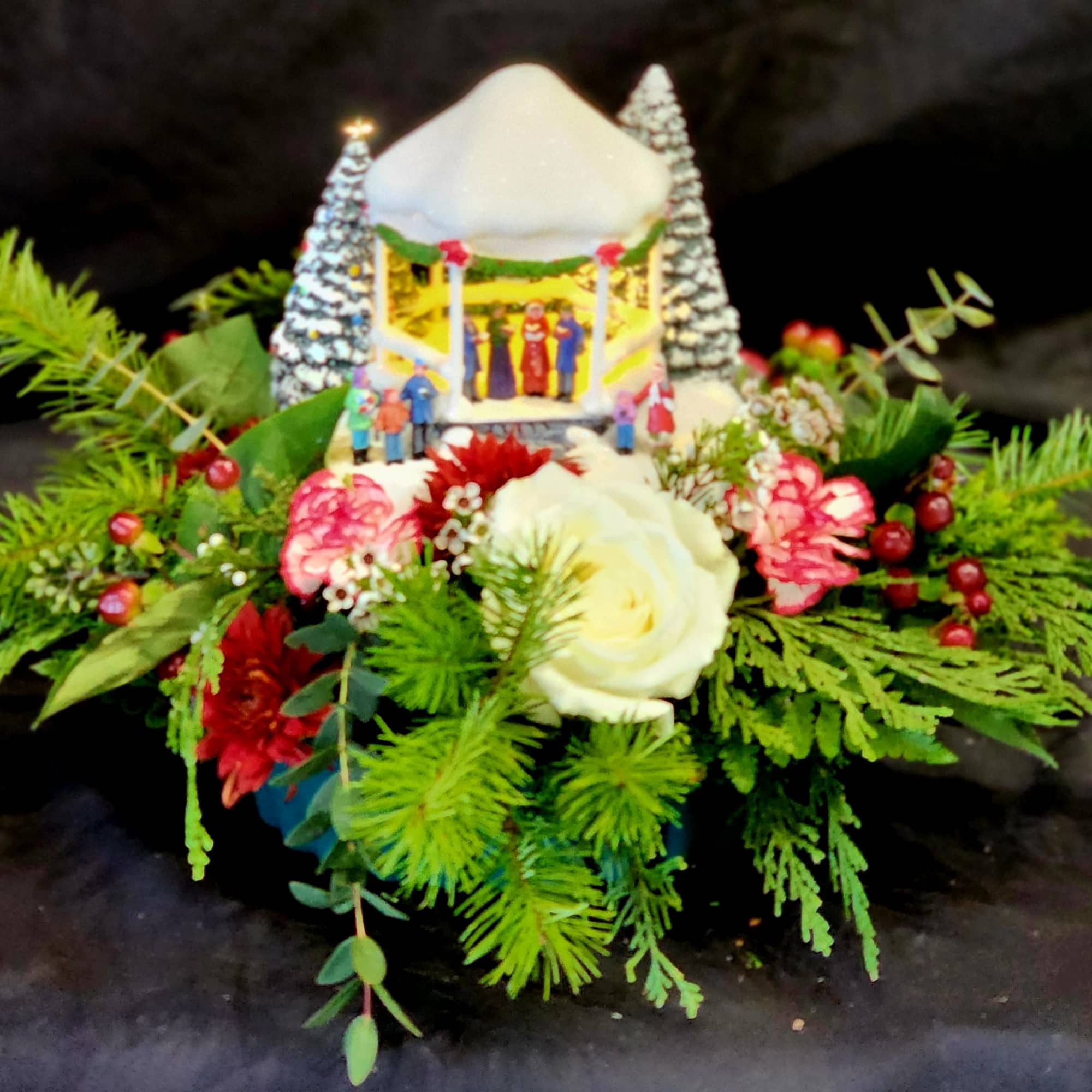 A Thomas Kinkaid keepsake that lights up, surrounded by evergreens, Hypericums, Roses