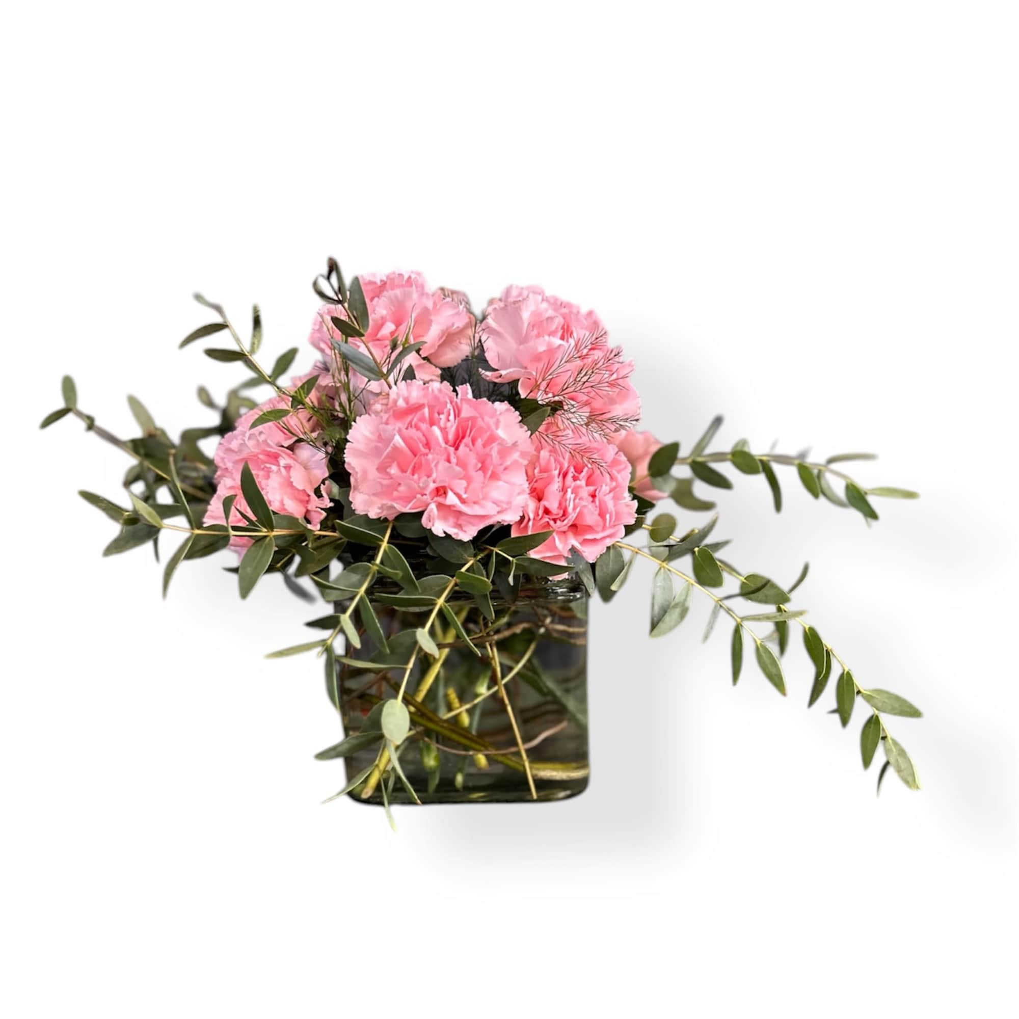 A dozen carnations designed in a cube vase among lush eucalyptus greenery.