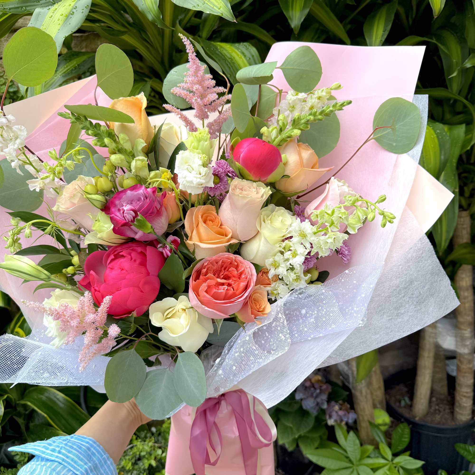 Hand-tied bouquet of bright pink peonies and mixed roses wrapped in pink paper with ribbon