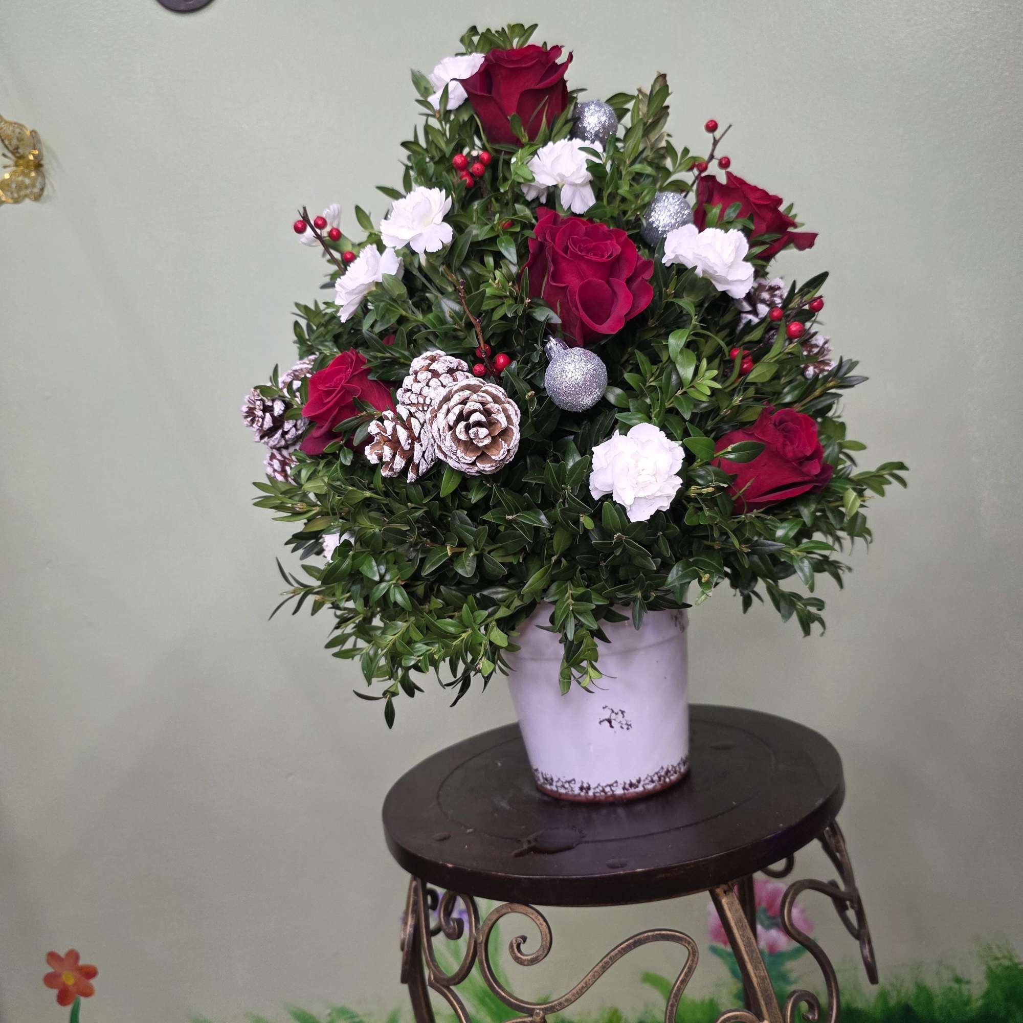 Festive Noel Rose Pot is a charming holiday arrangement featuring lush evergreen
