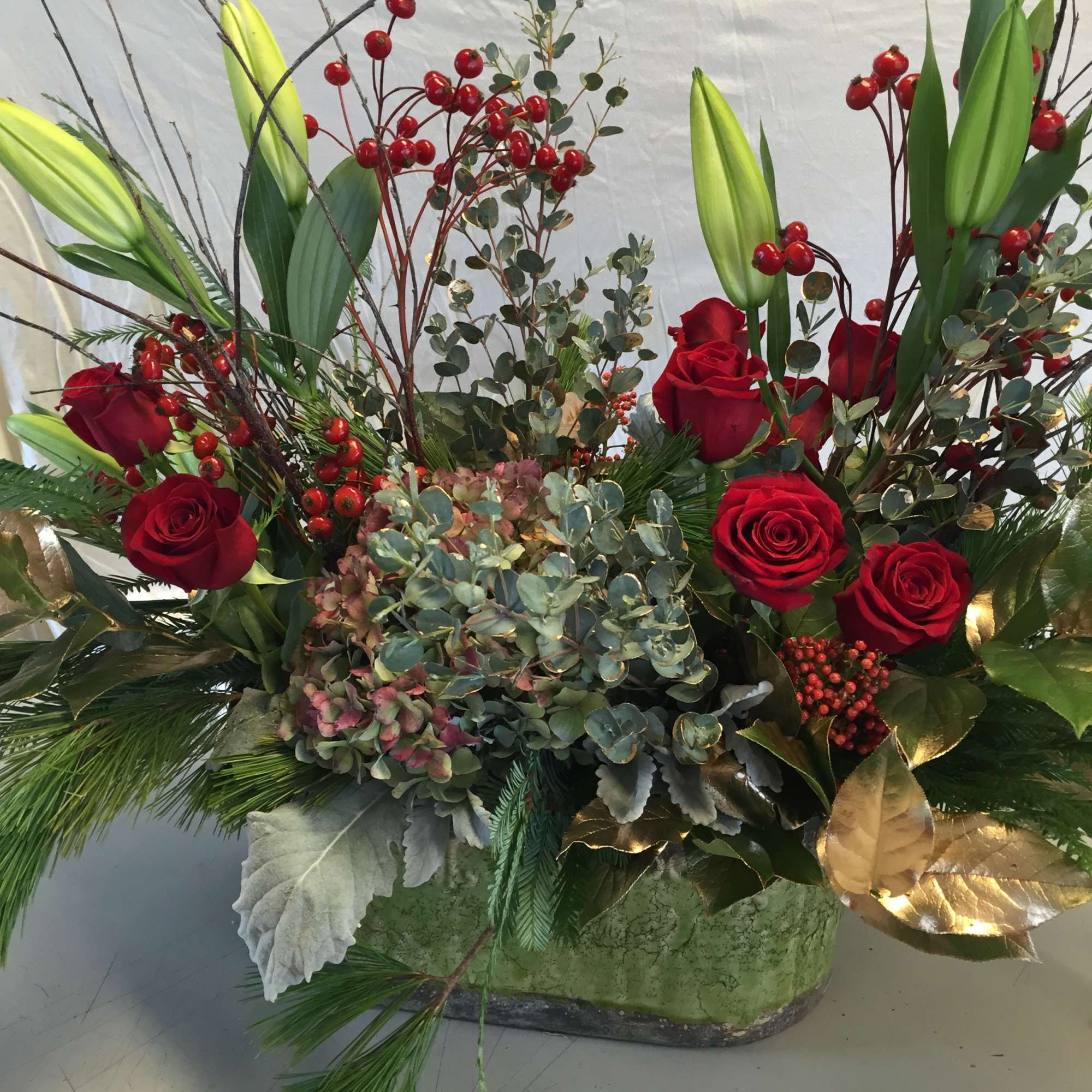 A large rustic-finish ceramic container contains a profusion of holiday evergreens, red