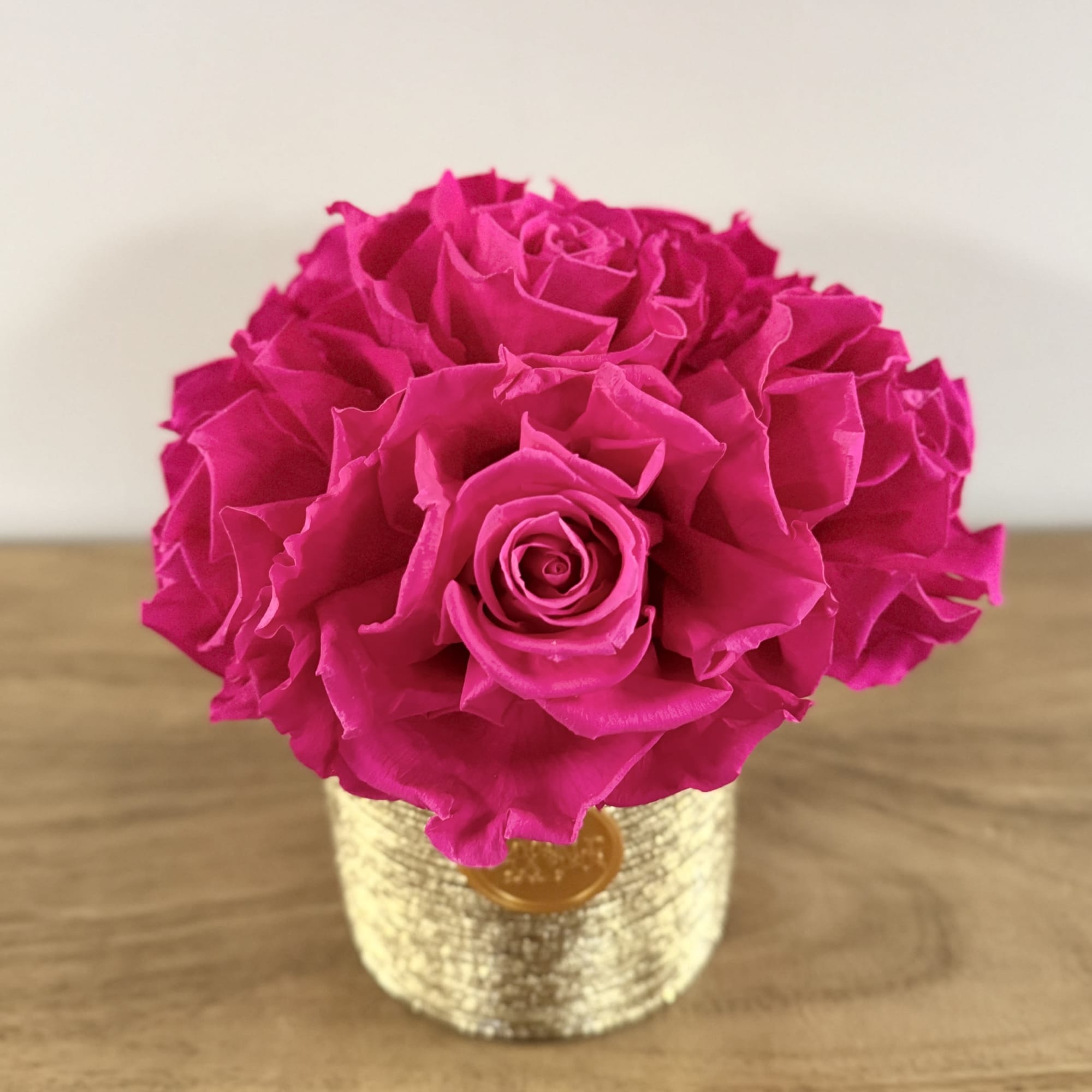 Six vibrant preserved fuchsia roses, thoughtfully arranged in a luminous gold vessel.