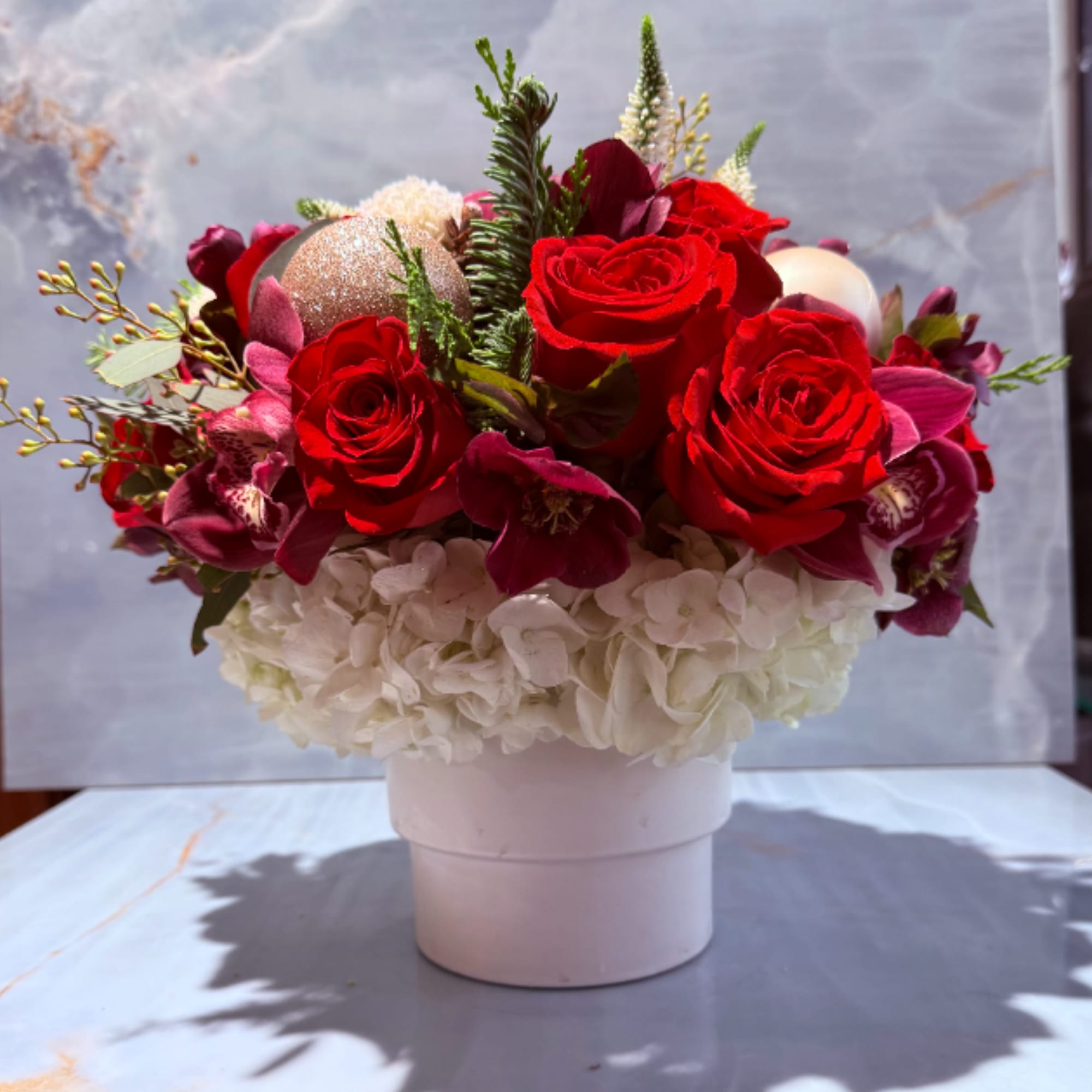 This arrangement consists of burgundy blooms, red roses, and evergreen foliage with