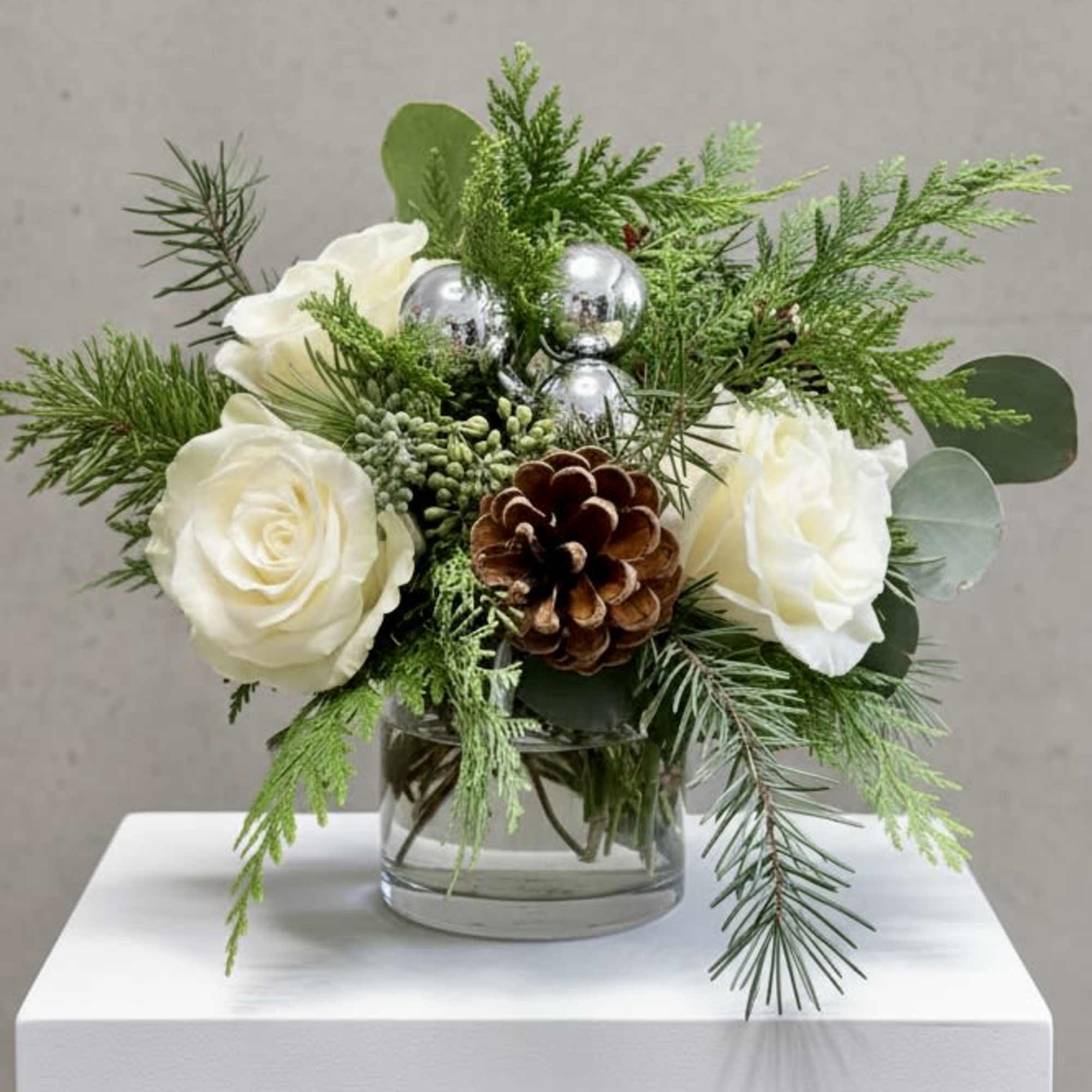Our wintery arrangement of white roses, silver balls and pinecones among a