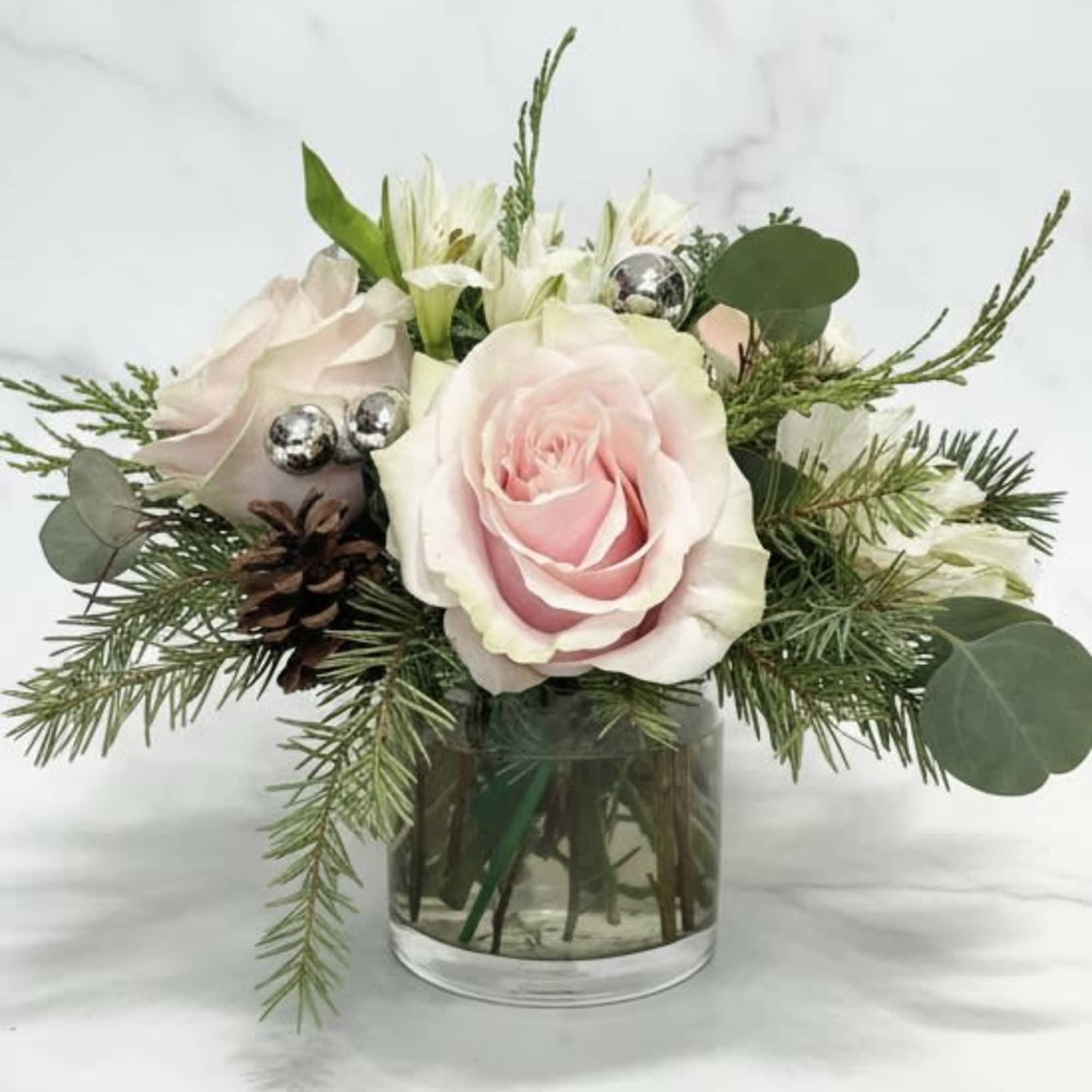 Our wintery arrangement of white roses, silver balls and pinecones among a