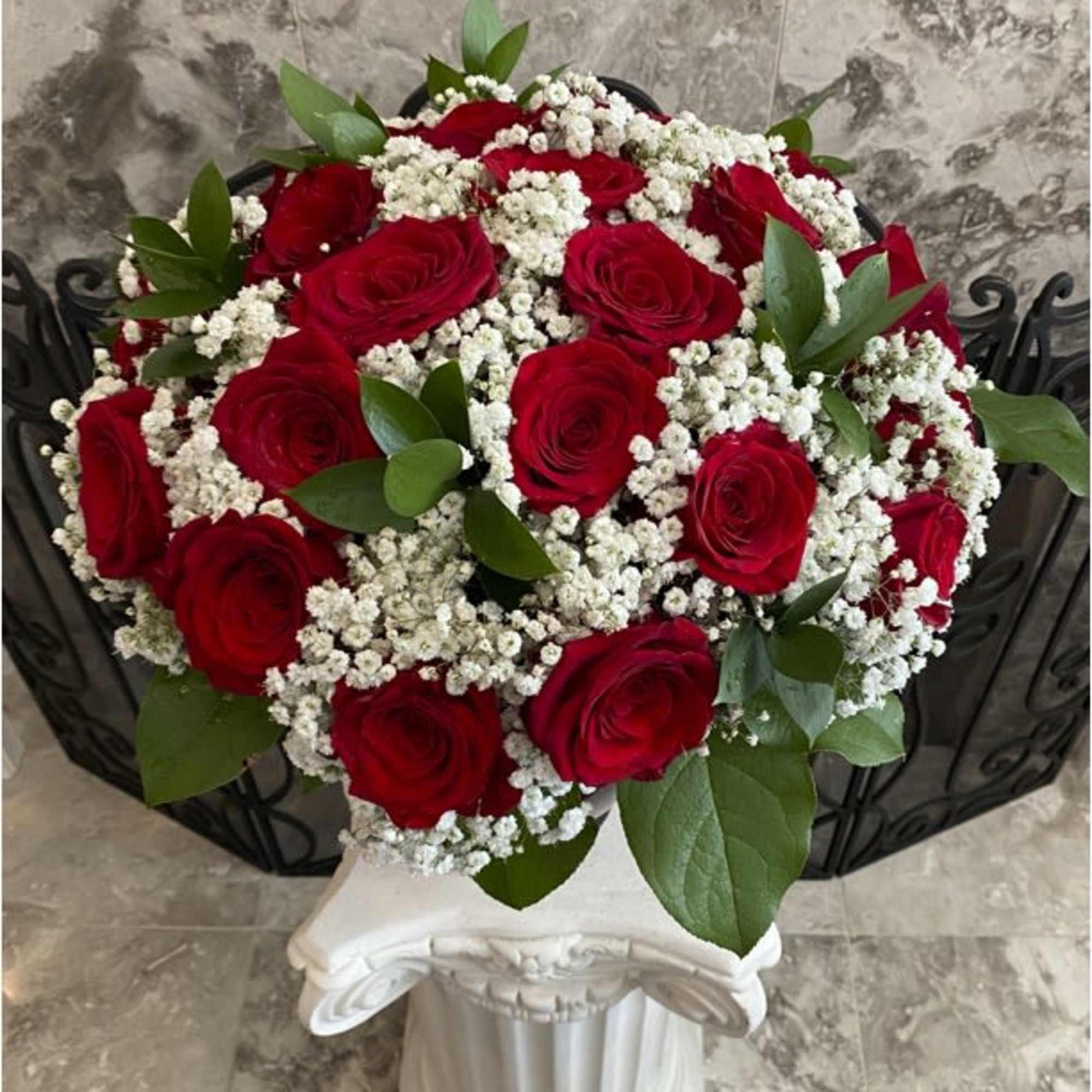A lavish bouquet of two dozen enchanting red roses, interspersed with delicate