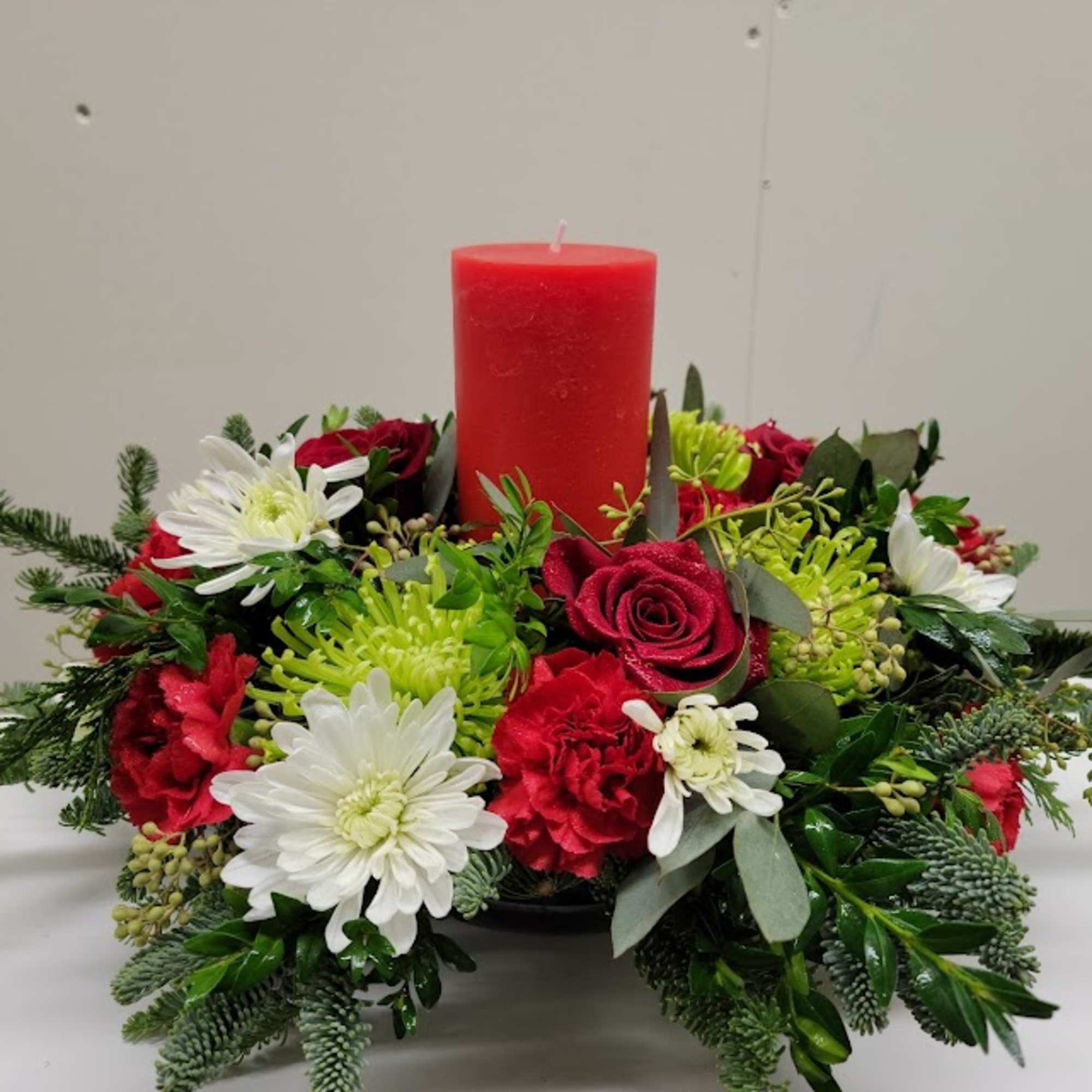 Modern Pillar candle centerpiece made with an assortment of evergreens, red roses