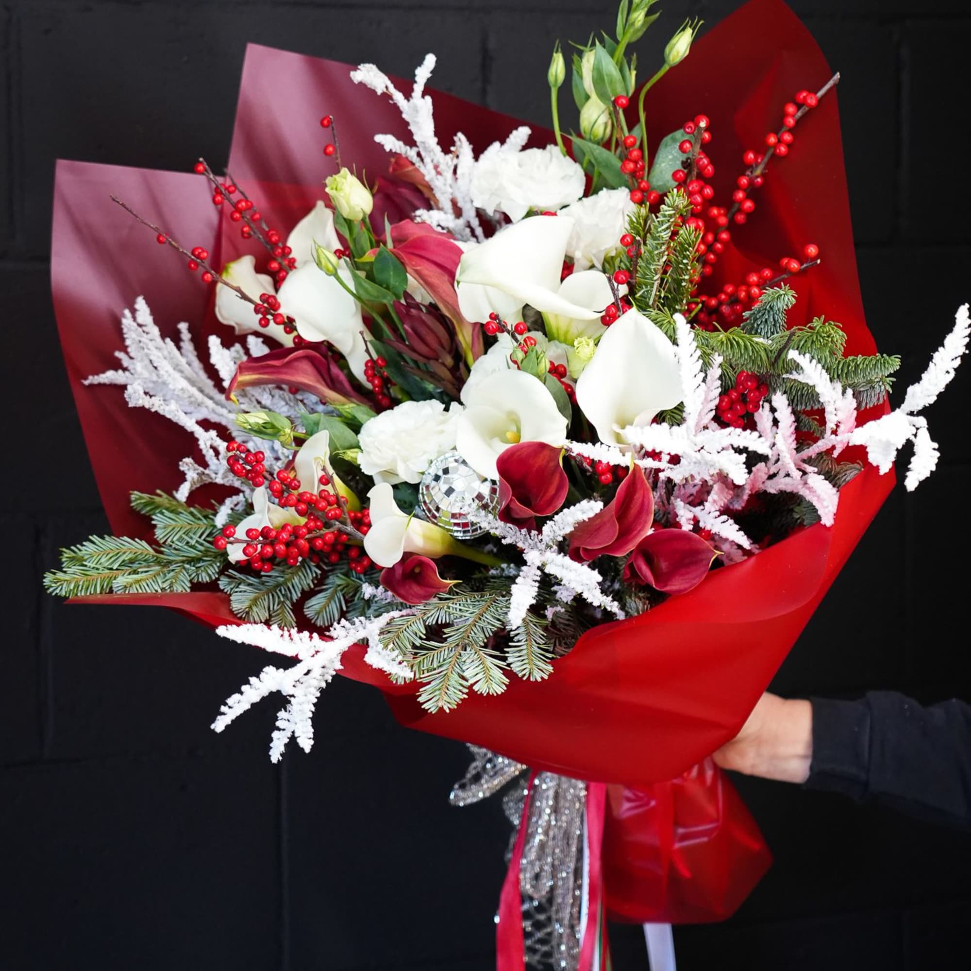 The Crimson Frost Bouquet is a dazzling holiday arrangement that captures the