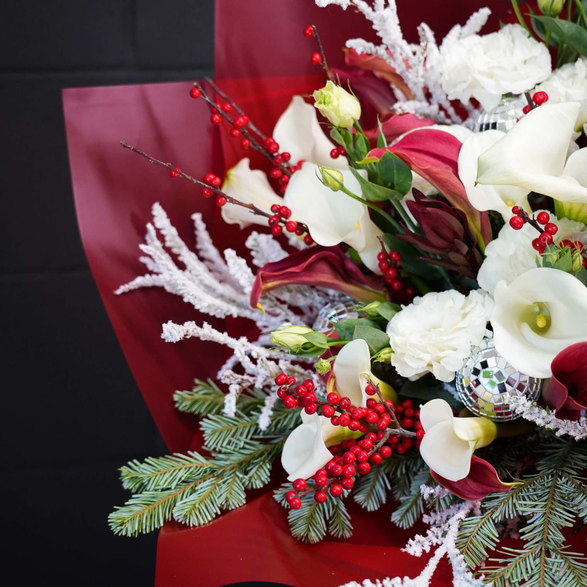 The Crimson Frost Bouquet is a dazzling holiday arrangement that captures the