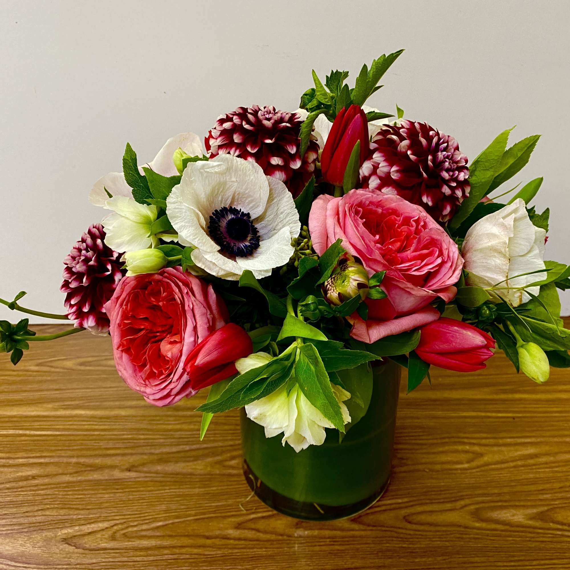 In a clear glass vase combinations of dahlia,  garden roses, tulips