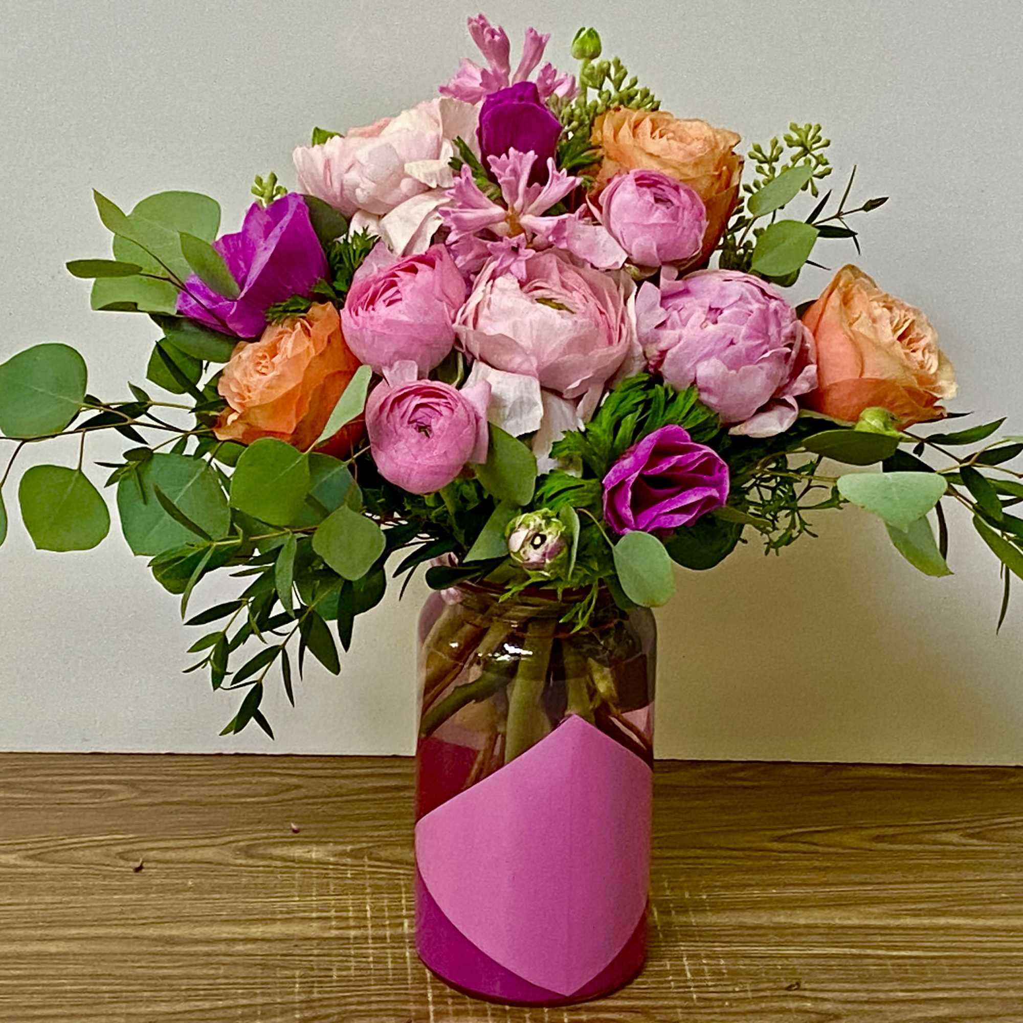 In a beautiful pink glass vase combinations of ranunculus, roses, peony, anemone
