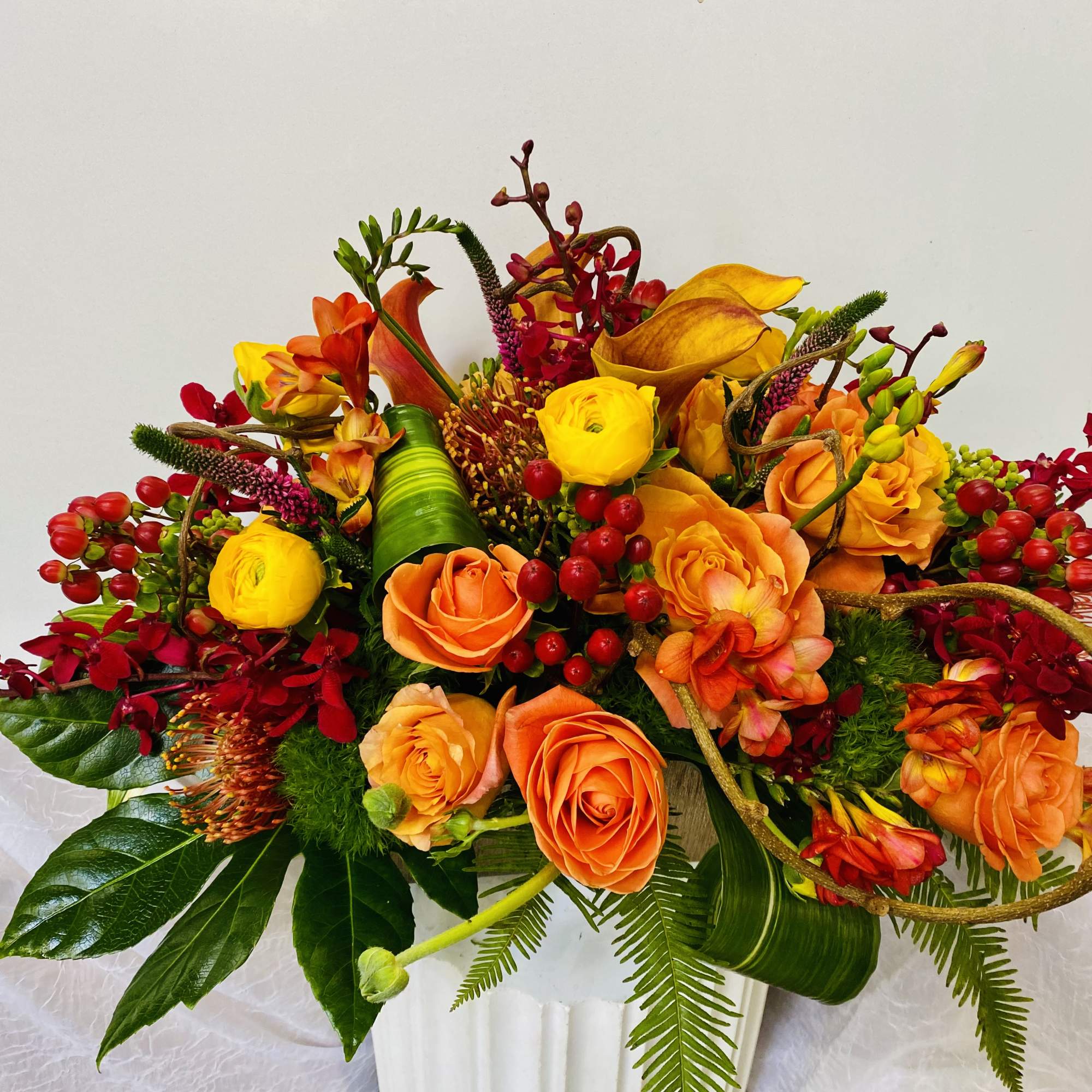 In a long vase combination of red roses, yellow roses, burgundy orchids