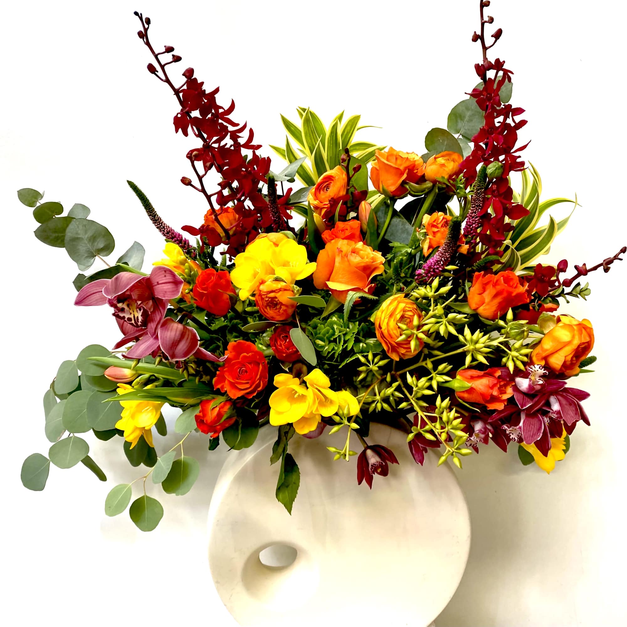 In a long vase combination of red roses, yellow roses, burgundy orchids