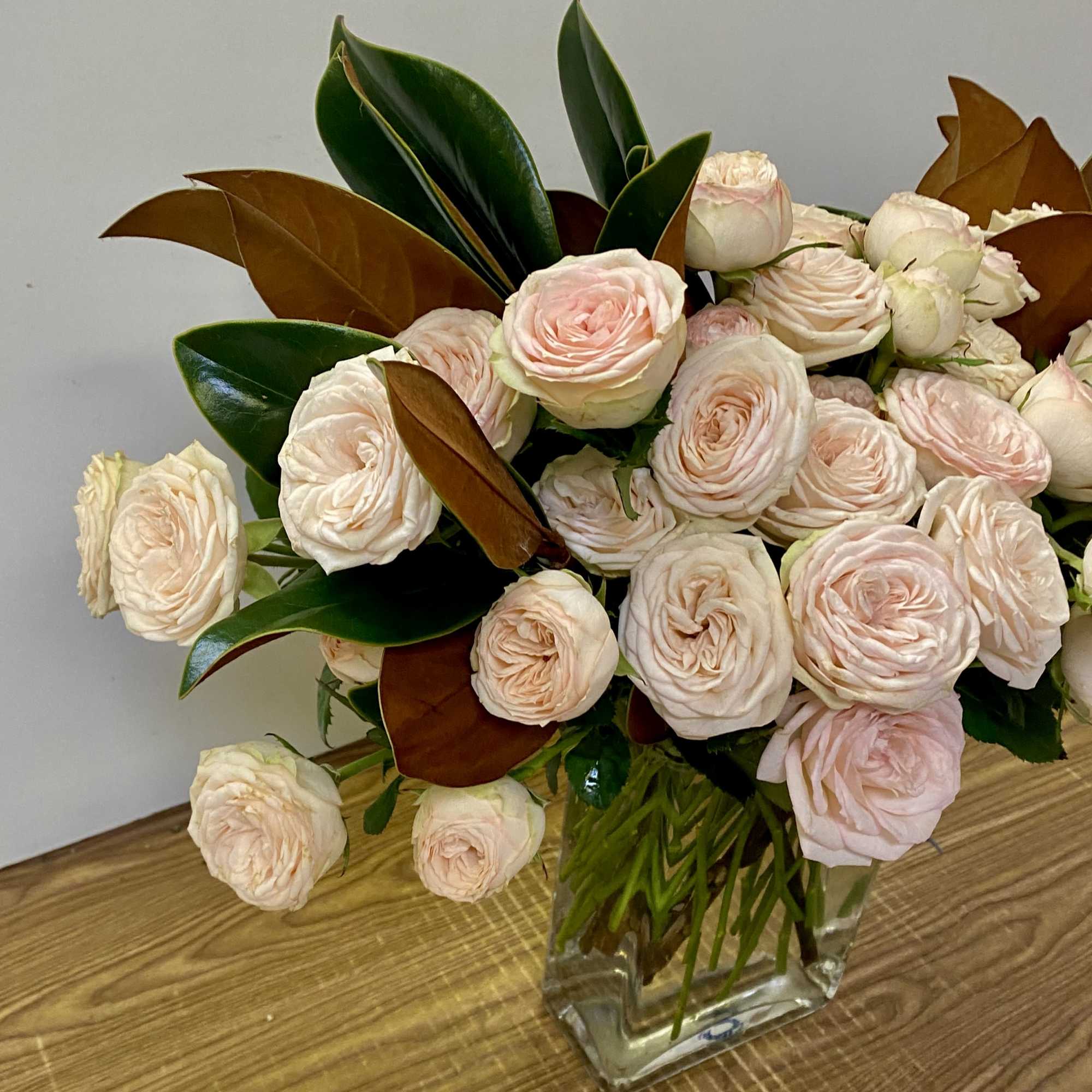 In a glass vase combination of Garden yellow roses with magnolia leaves