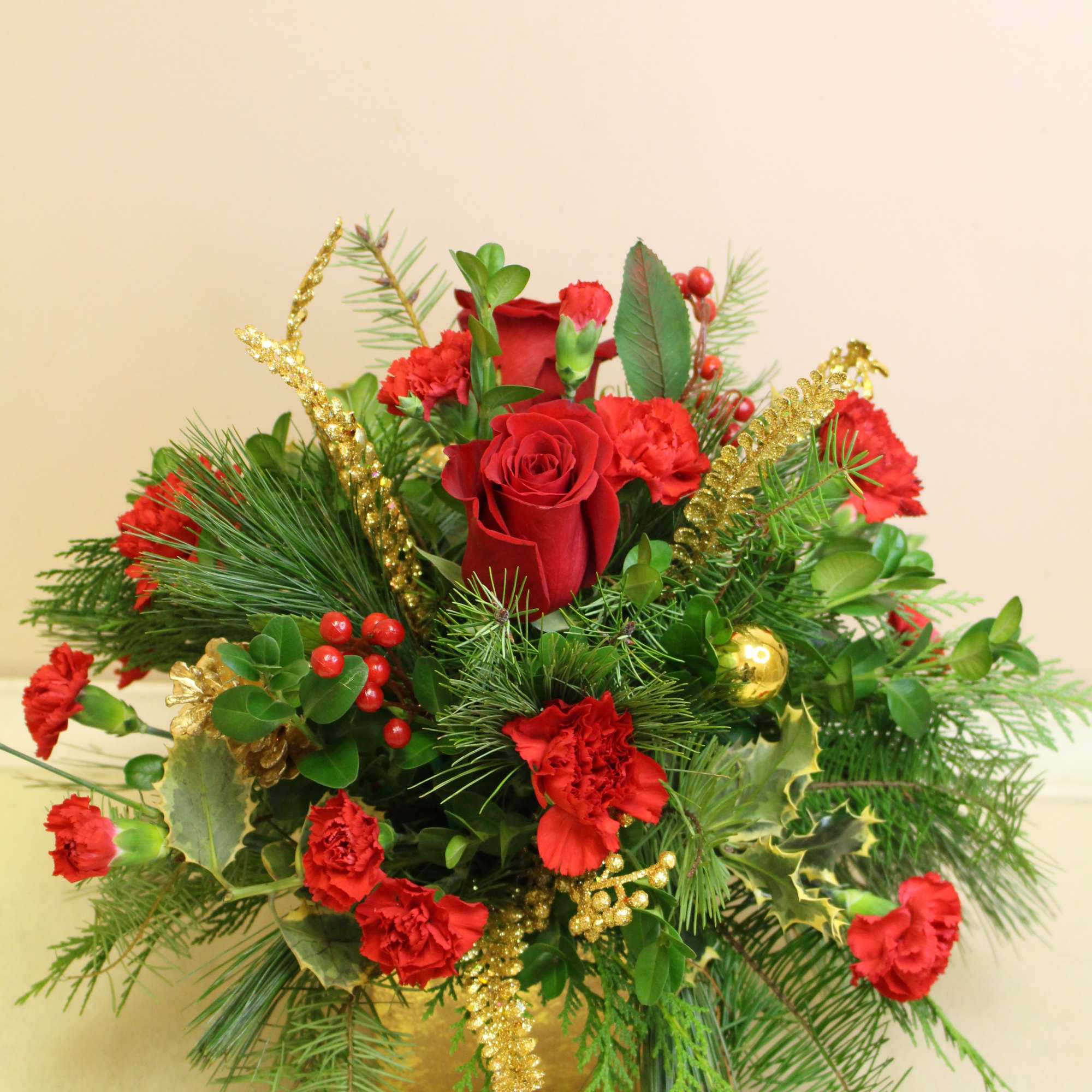 A gold ceramic cube, filled with a mix of fresh Christmas greens.