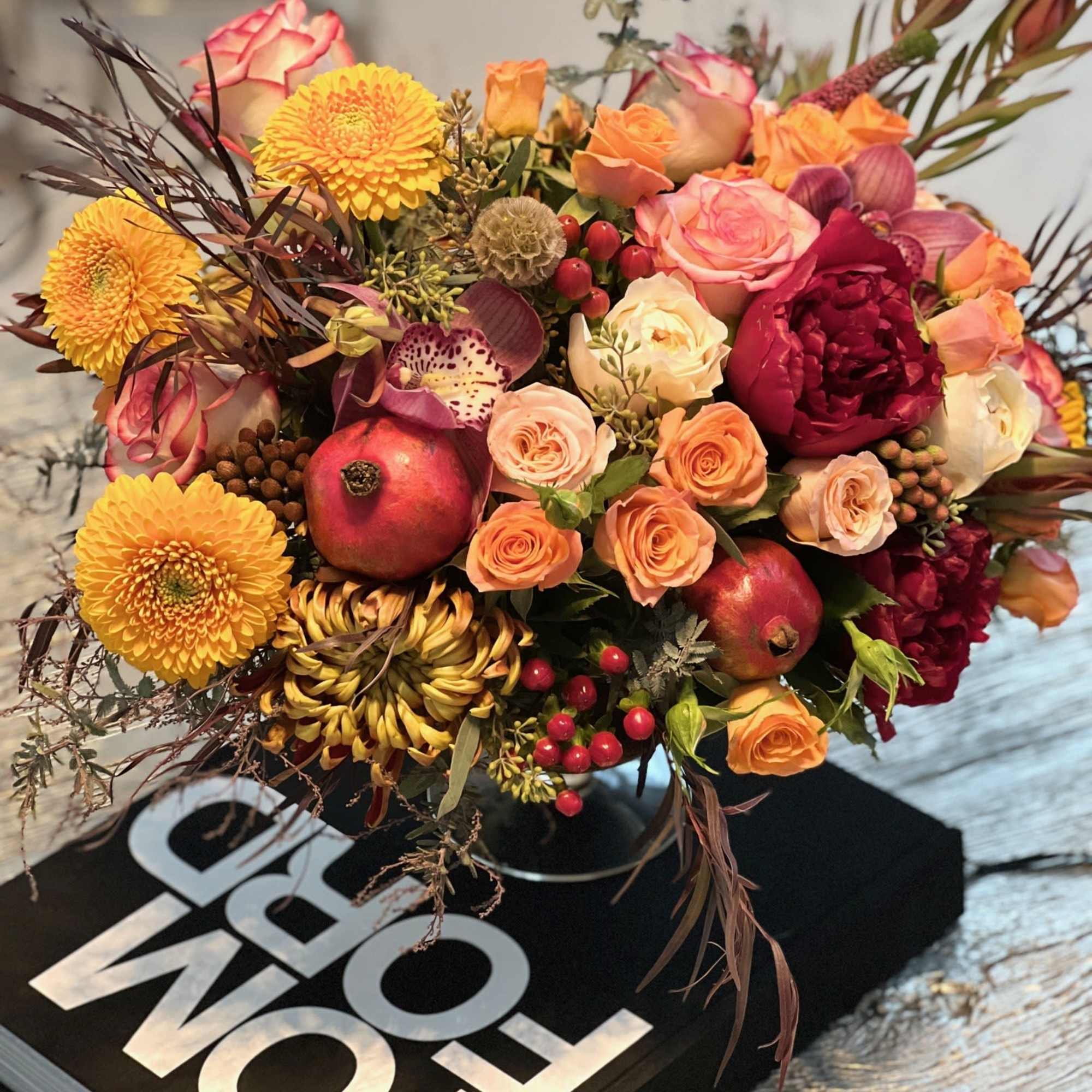 This opulent centerpiece bursts with autumnal charm, blending rich burgundy roses, golden