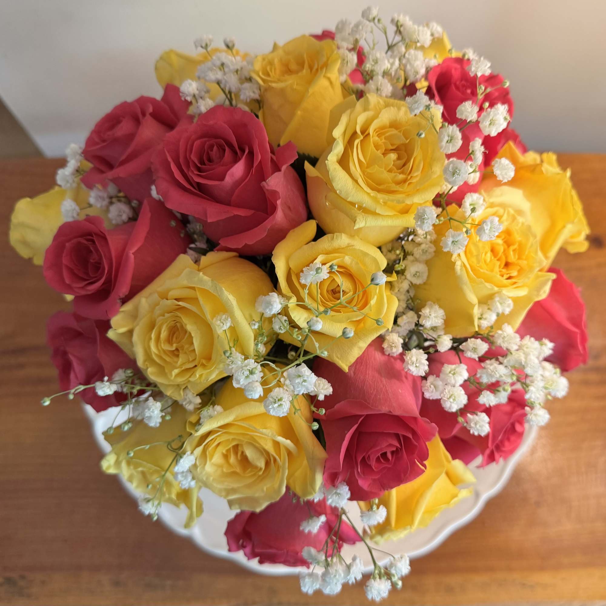 A lovely bowl of 24 colorful roses and filler brightens and lifts