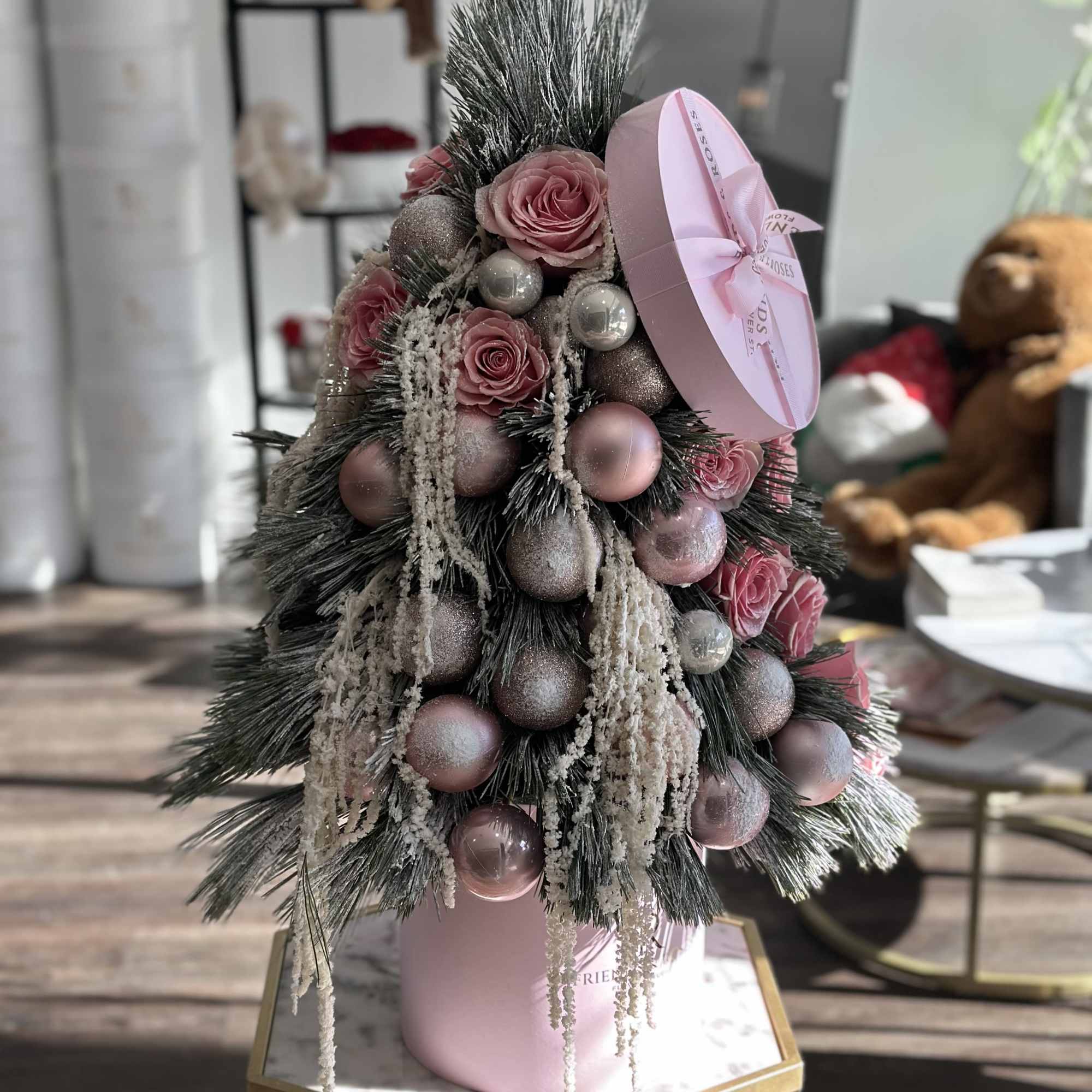 An elegant holiday arrangement featuring soft pink pink roses, festive ornaments, and