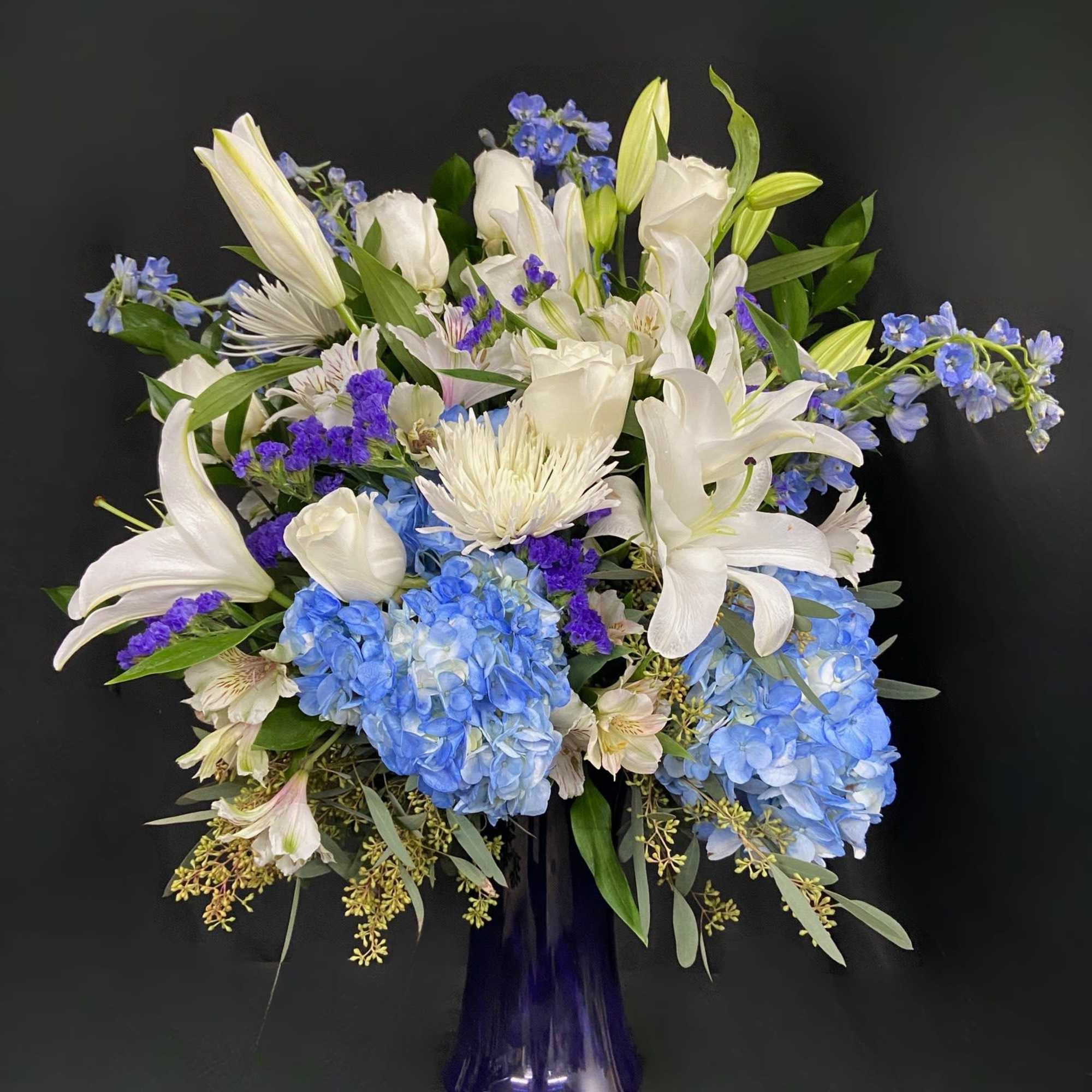 This peaceful arrangement includes roses, oriental lilies, fuji mums, blue delphinium, blue