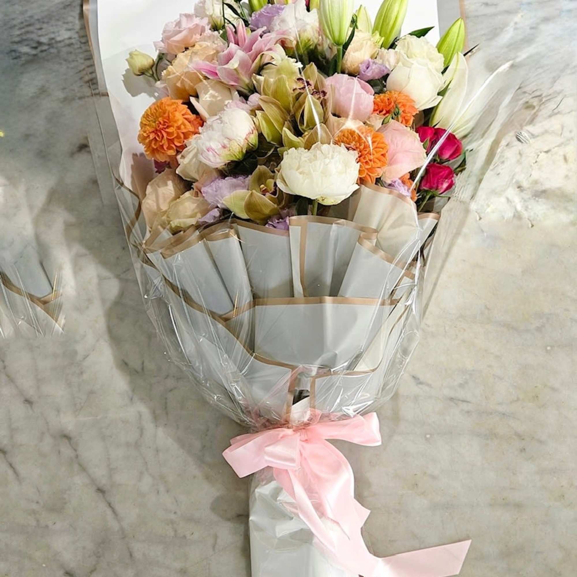 This premium wrap bouquet features dahlias, peonies, rose lilies, spray roses, cymbidium