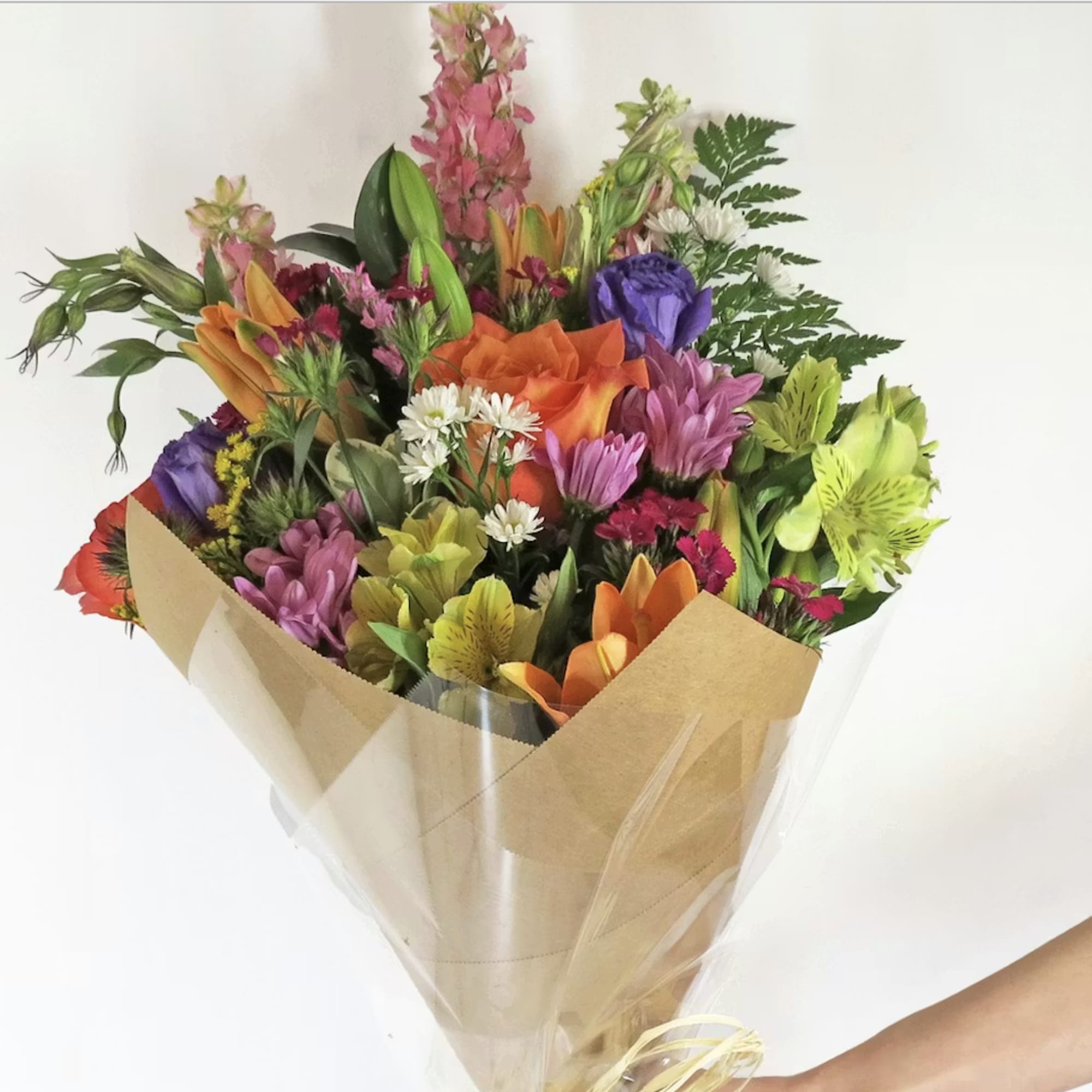 assorted seasonal fresh flowers wrapped in paper with greenery and bow. Add