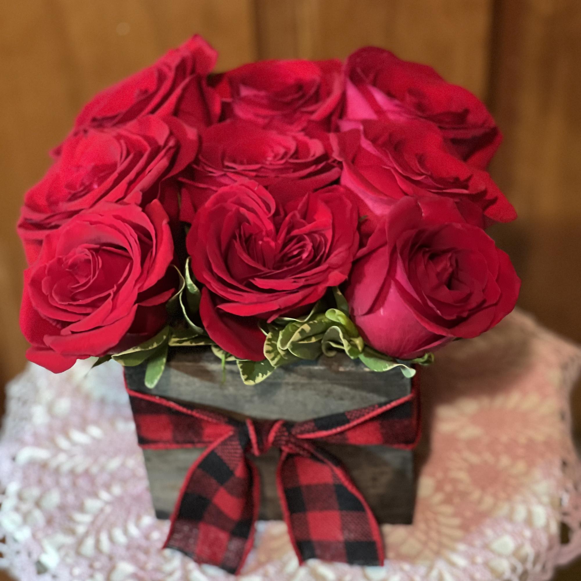 9 roses nestled into a wooden box with variegated pittosporum, finished off