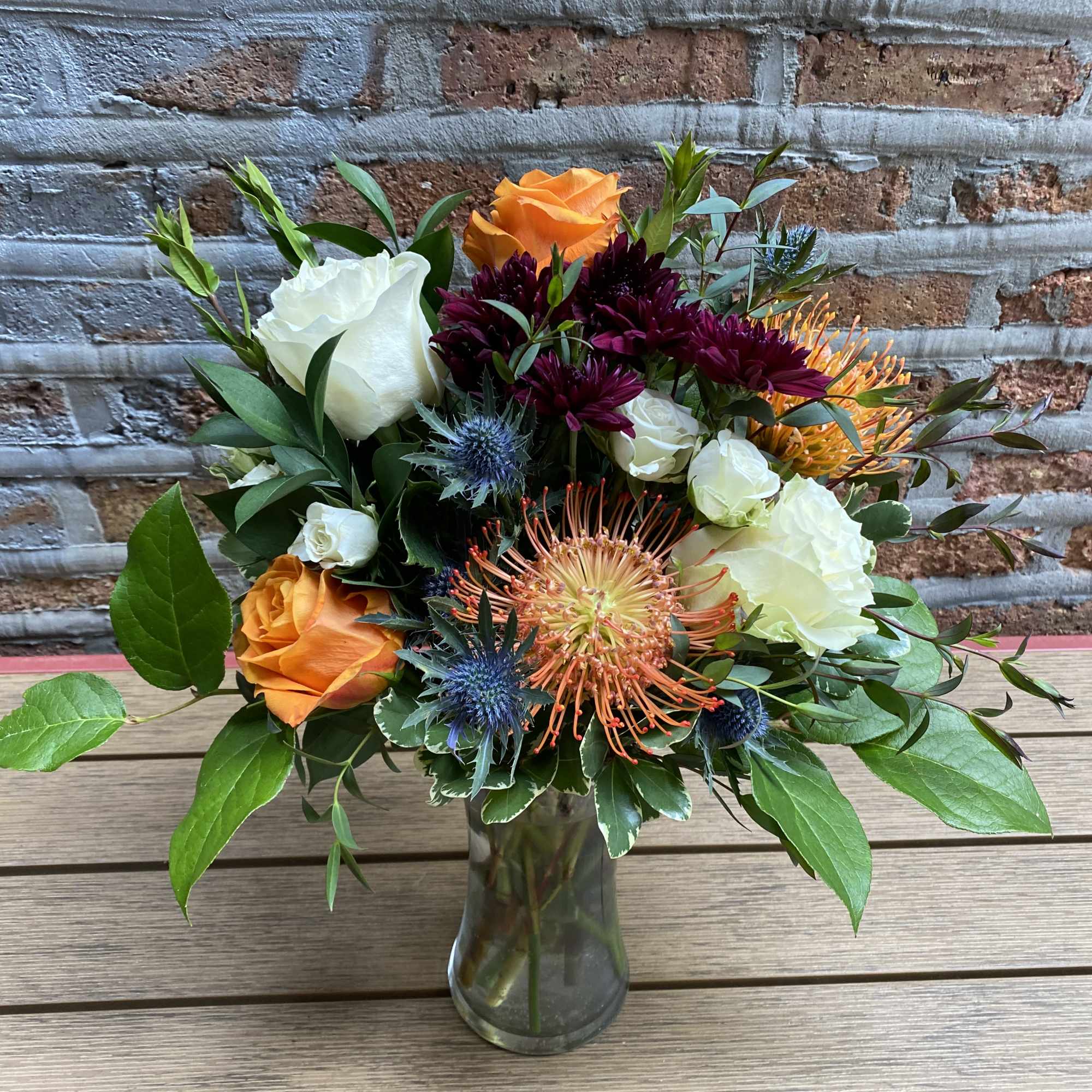 A Modern Arrangement of Orange Pin Cushions and Thistle and Vibrant Greens